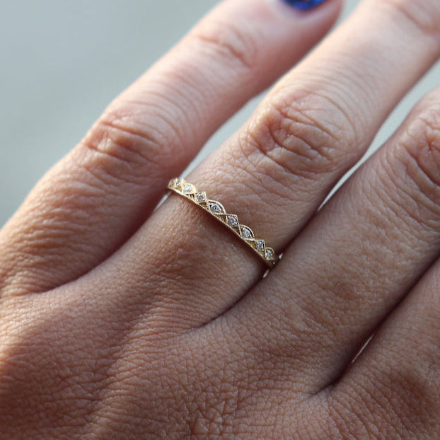 A hand with blue patterned nails wears the DMD Metal Emille Eternity Ring, a thin 14K gold band, on the middle finger.