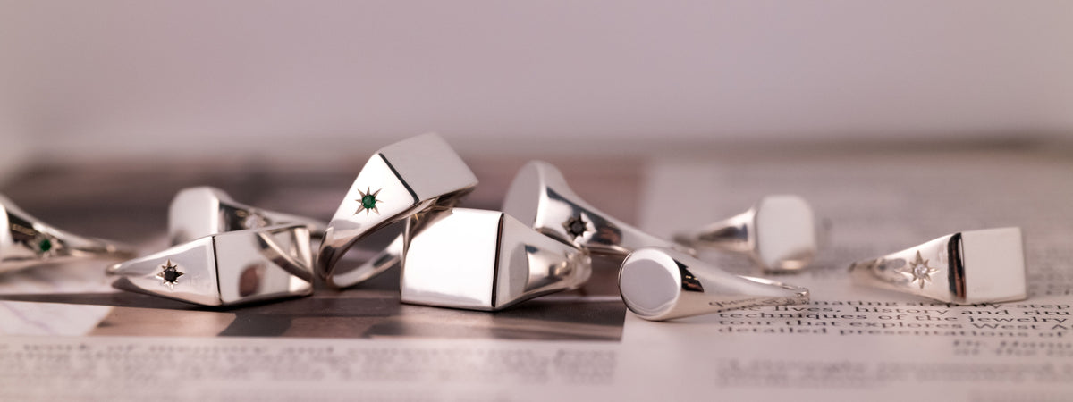 A collection of silver signet rings, some featuring small inset stones or star-shaped engravings, arranged on a printed page.