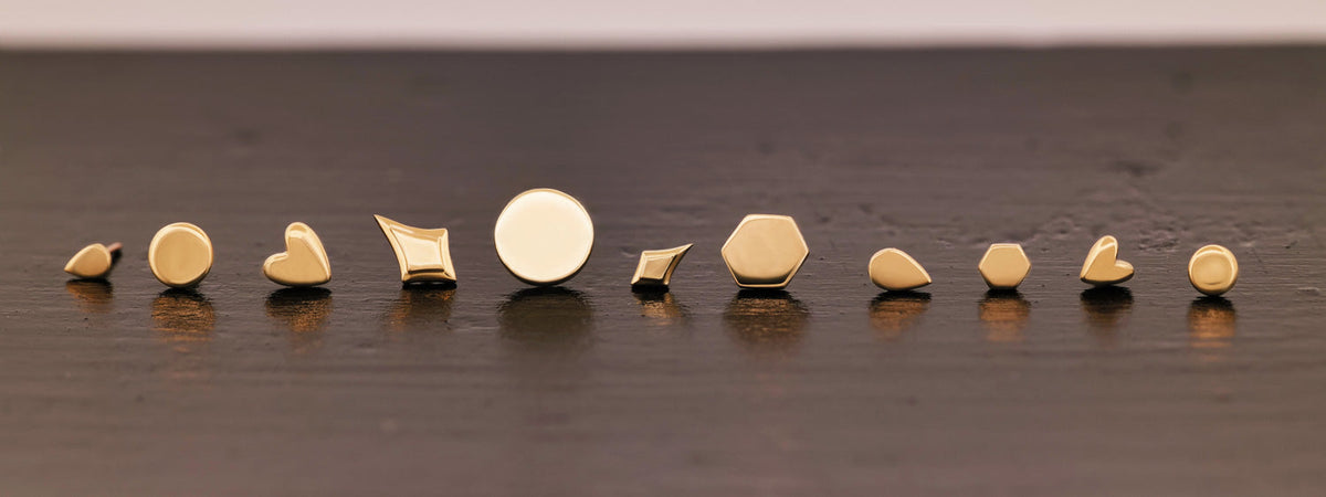 Ten gold stud earrings in various geometric shapes lined up on a dark surface.