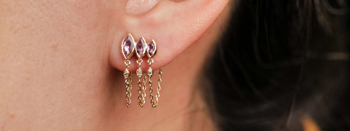 A gold ear climber earring featuring three marquise-cut pink gemstones, each with a dangling gold chain.