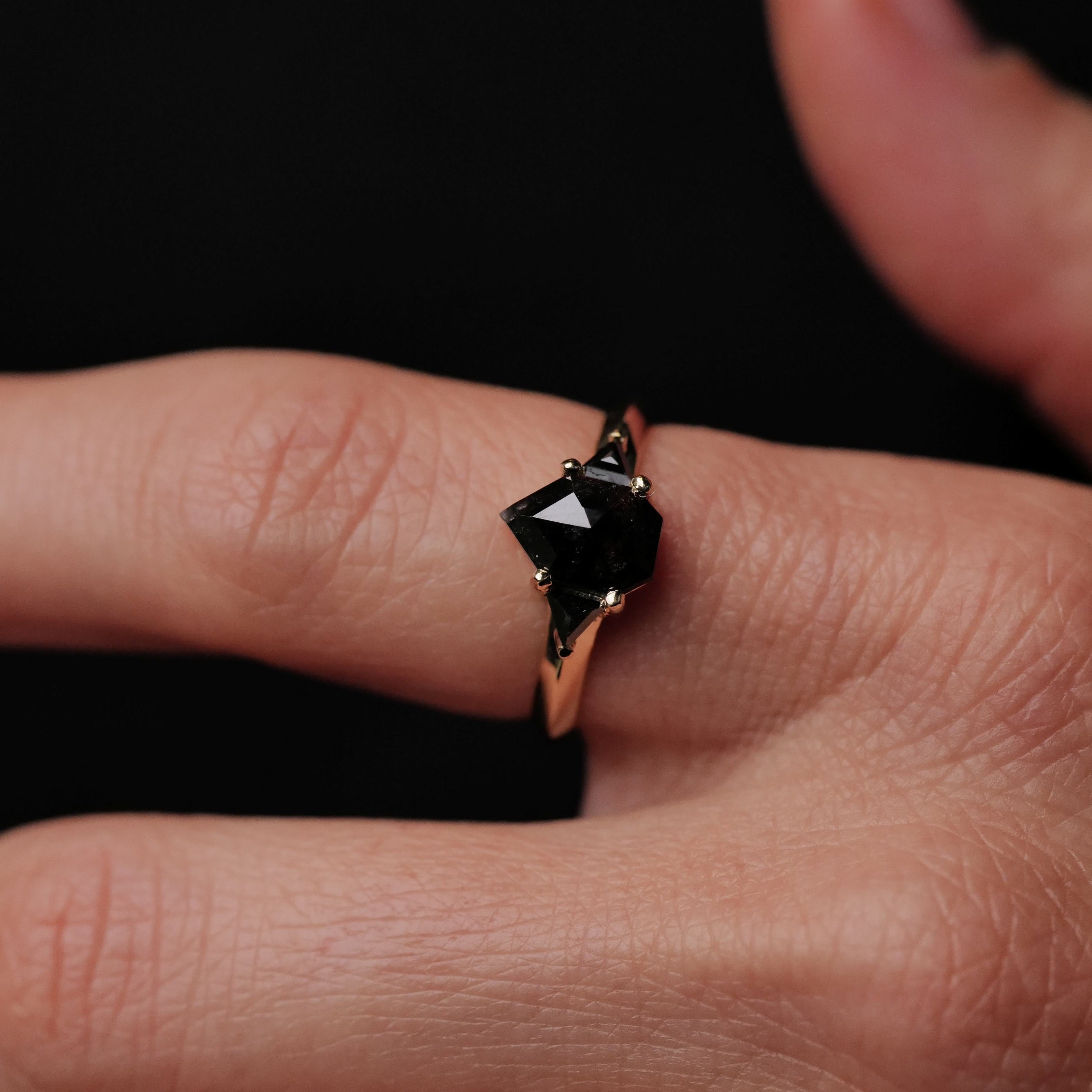 A hand wears Digby & Iona’s Petite Caliburn - Black Diamonds (1.62ct) ring on the middle finger against a dark background.