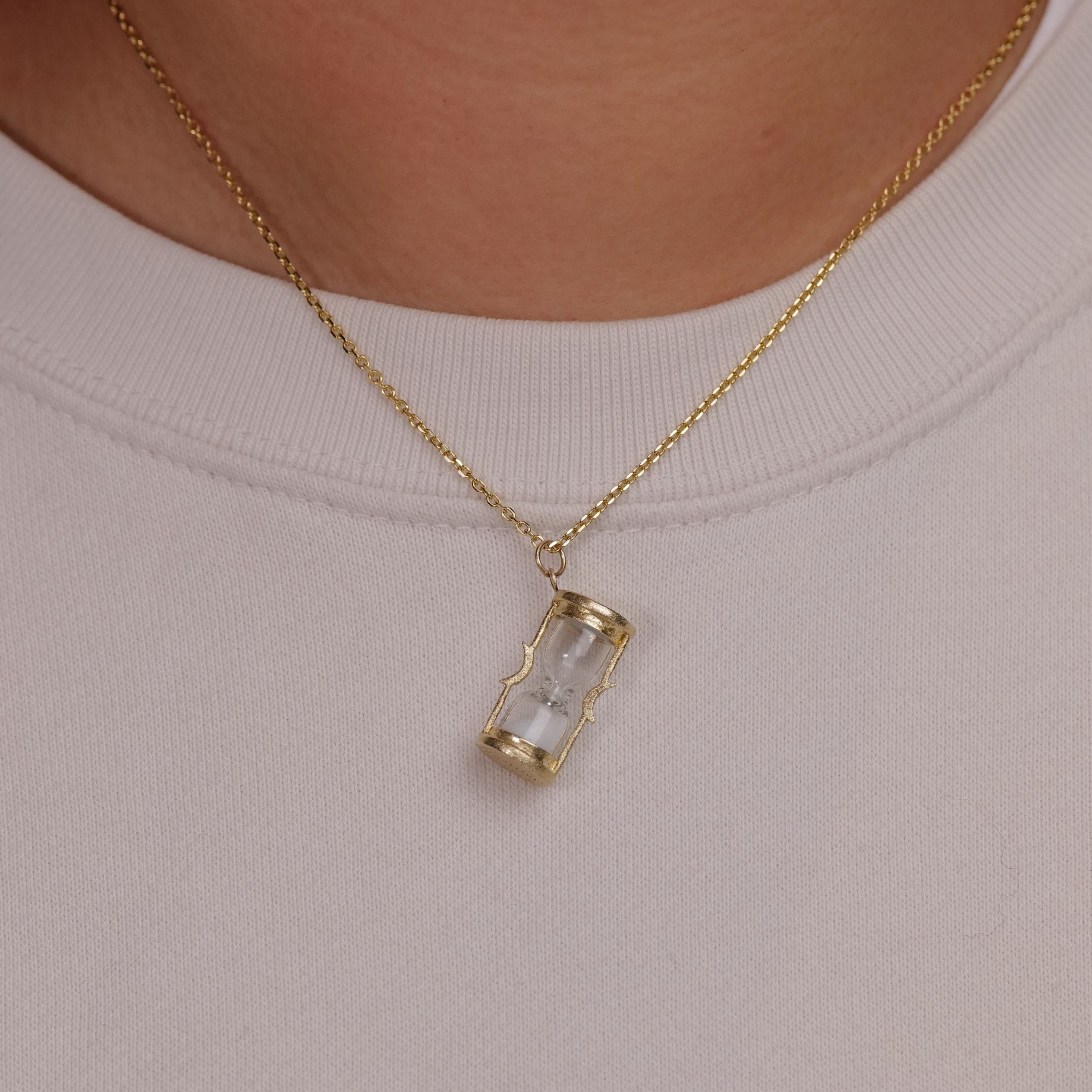 An Acanthus Sands of Time Hourglass Charm necklace in 14k gold rests elegantly on a light-colored shirt.