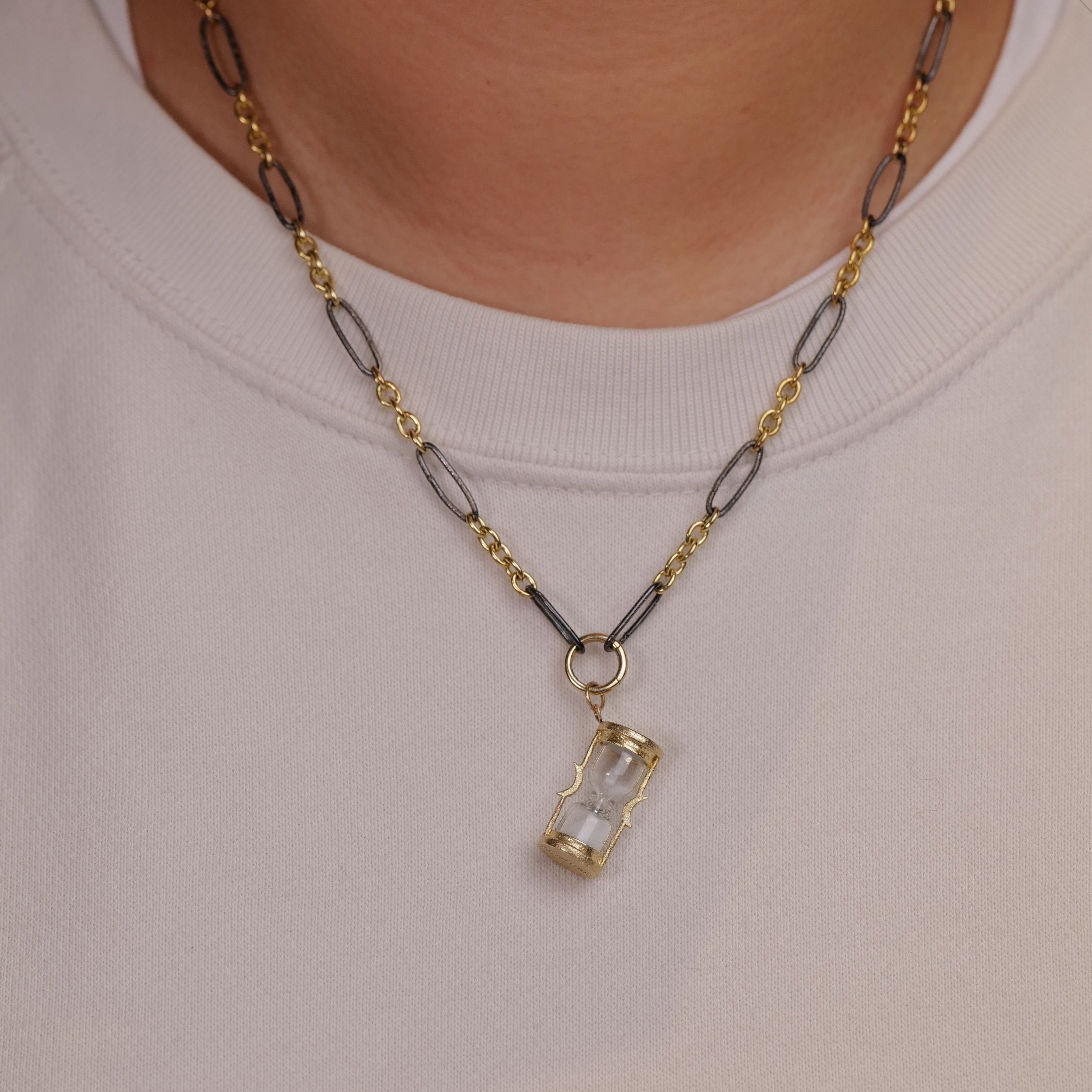 Acanthus Sands of Time Hourglass Charm pendant on gold and silver chain, styled over a light shirt.