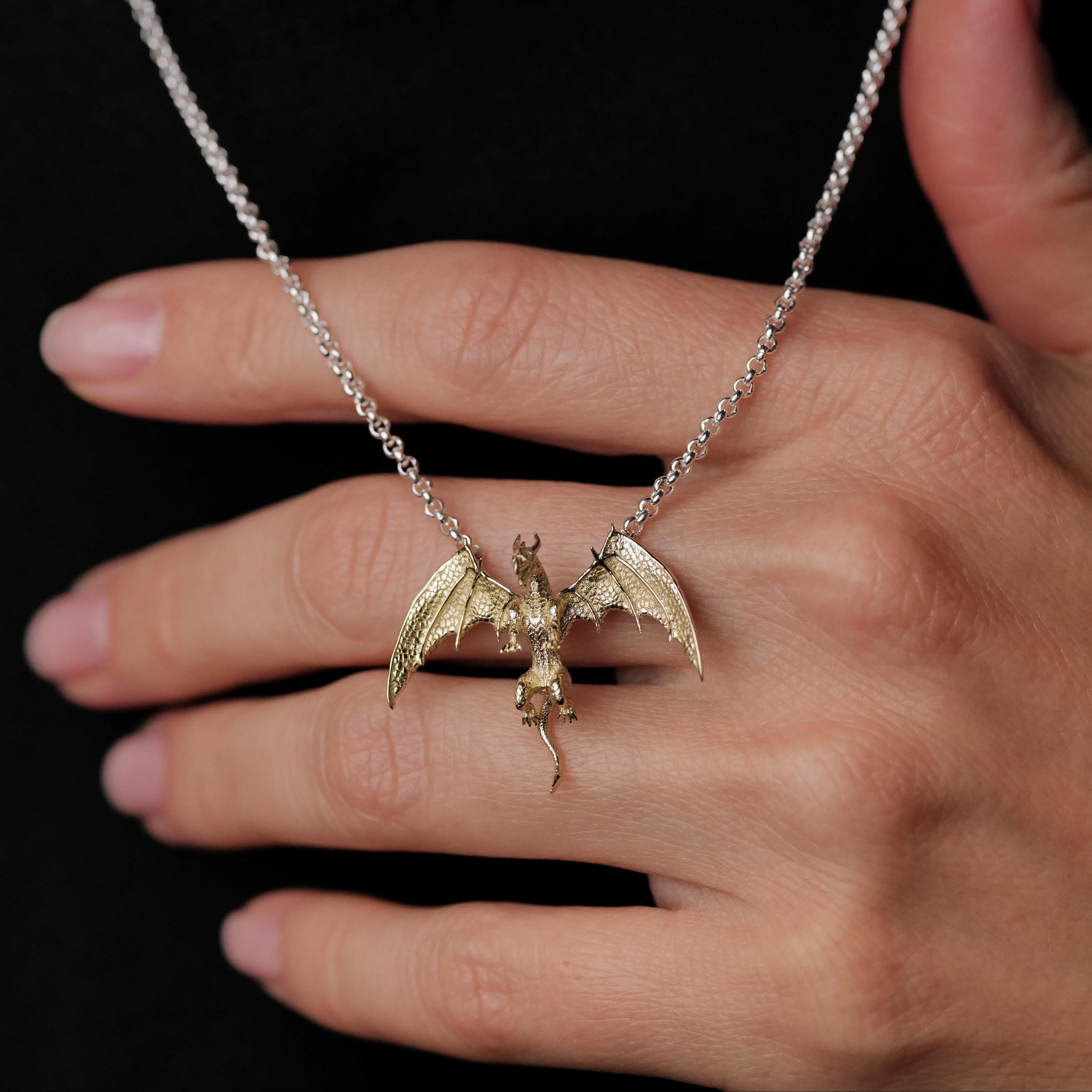 A hand holds the Fiat Lux Medieval Dragon Necklace (G), featuring a 10K gold charm, against a black background.