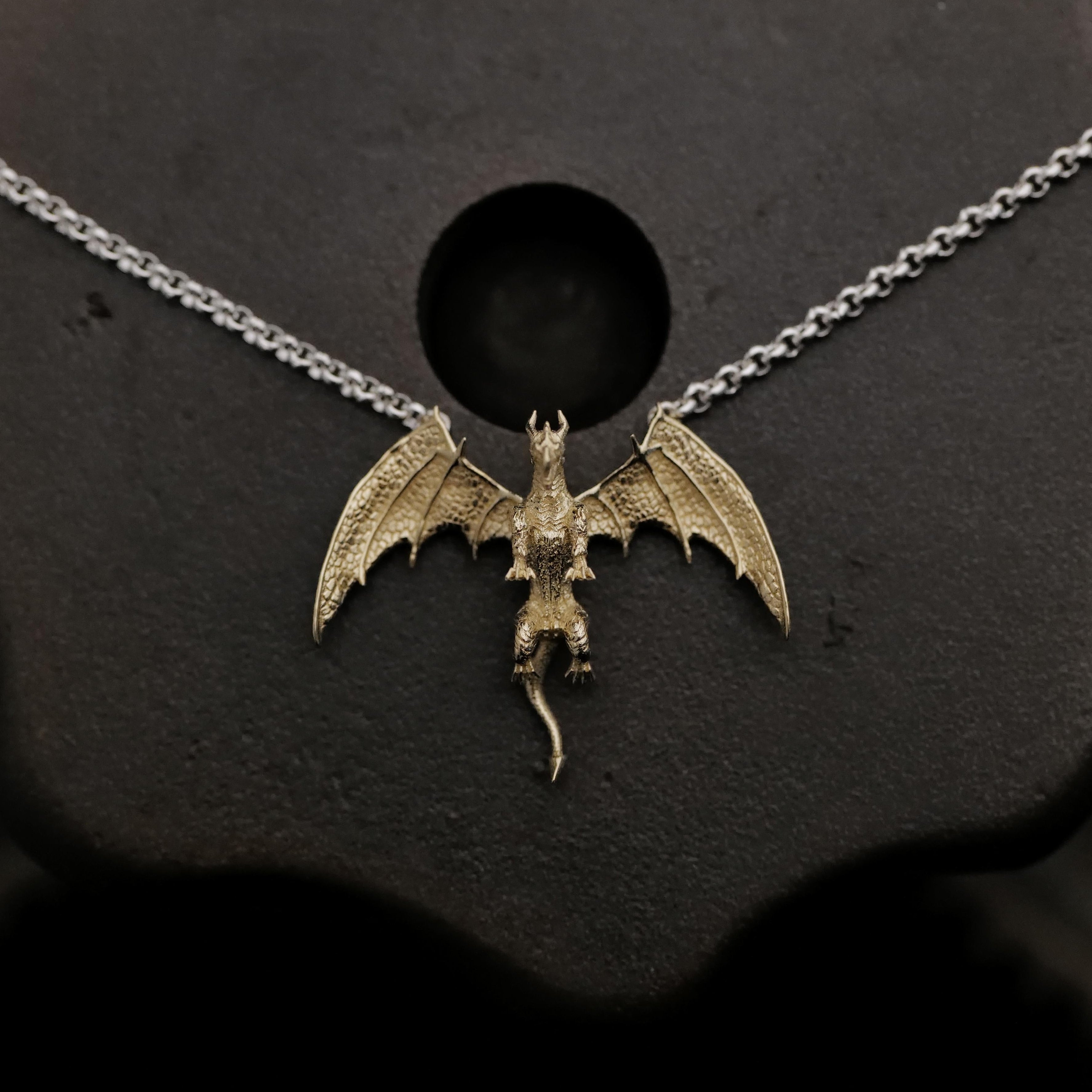The Fiat Lux Medieval Dragon Necklace (G) features a 10K gold dragon on a silver chain against a dark backdrop.