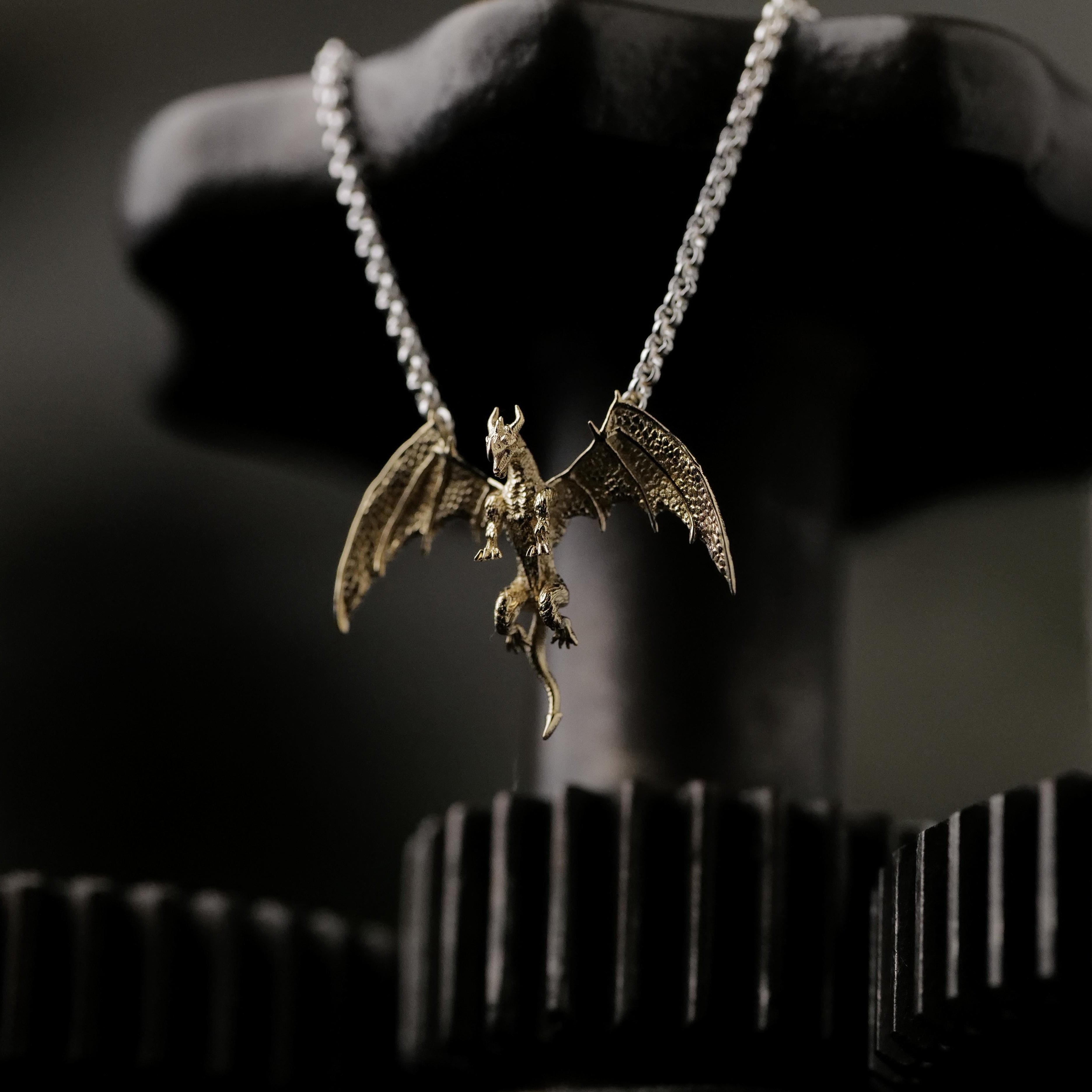 The Fiat Lux Medieval Dragon Necklace (G) shines against black metal gears with a dark, mysterious backdrop.
