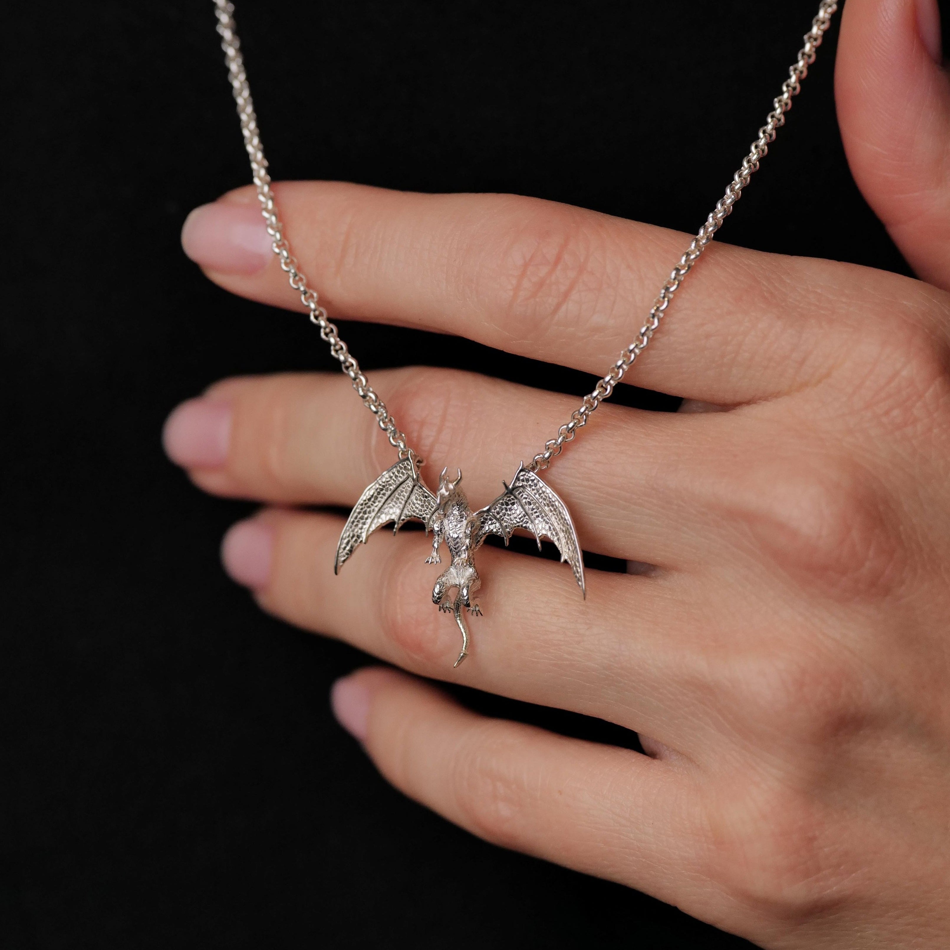 A hand touches the Fiat Lux Medieval Dragon Necklace (S) with a rune-etched charm on a black background.