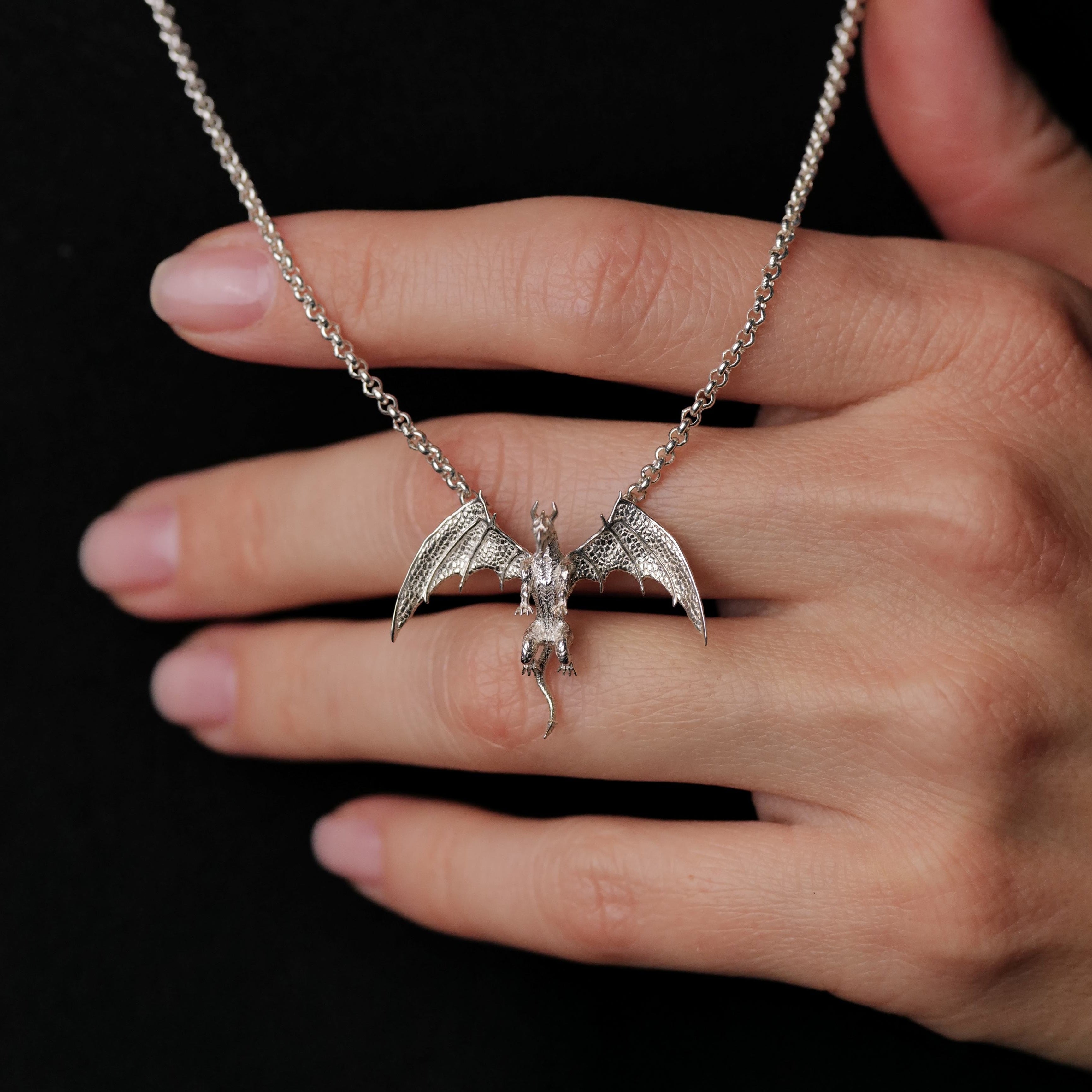 The Fiat Lux Medieval Dragon Necklace (S) in sterling silver is shown on a hand with a black background.