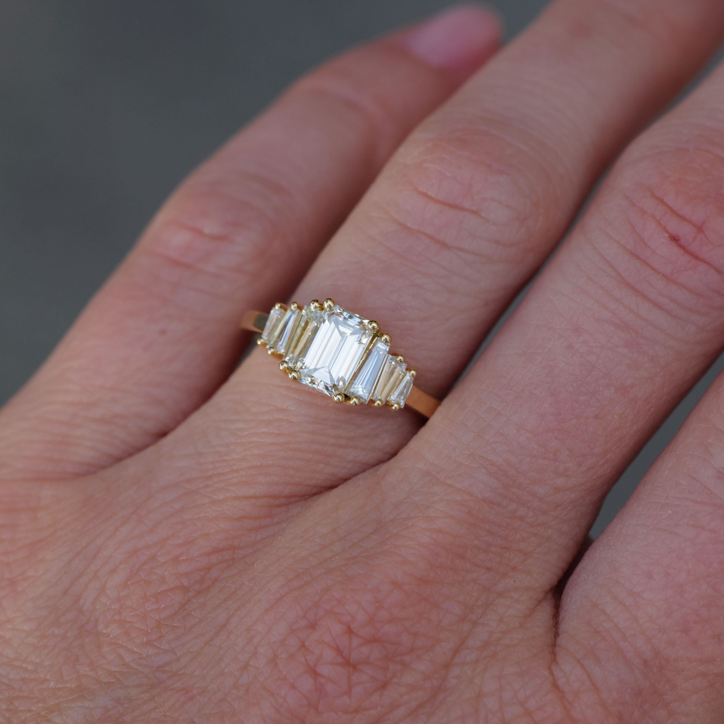 A Fiat Lux Classic Calypso 1.02ct emerald cut diamond ring is worn on a finger in close-up.