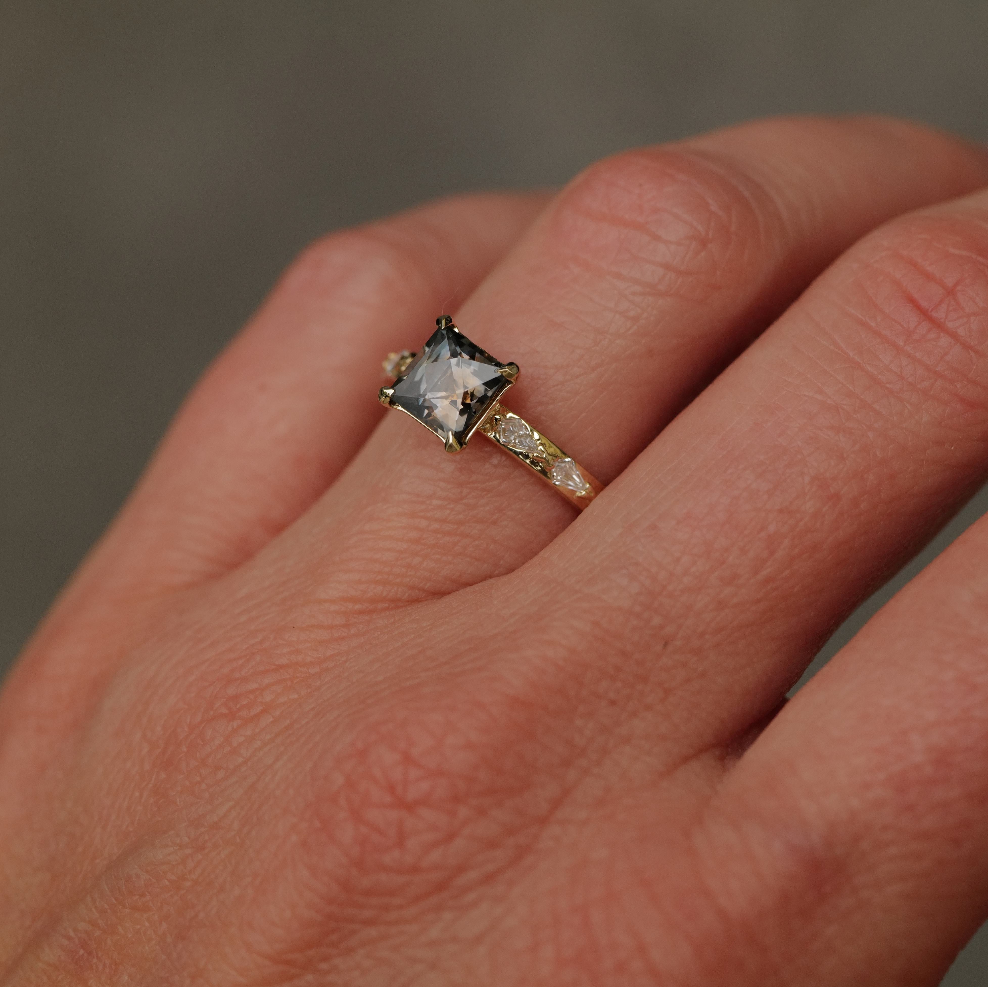 A hand wearing Fiat Luxs Classic Theia Ring with a square-cut plum sapphire and diamond-accented 14K gold band.