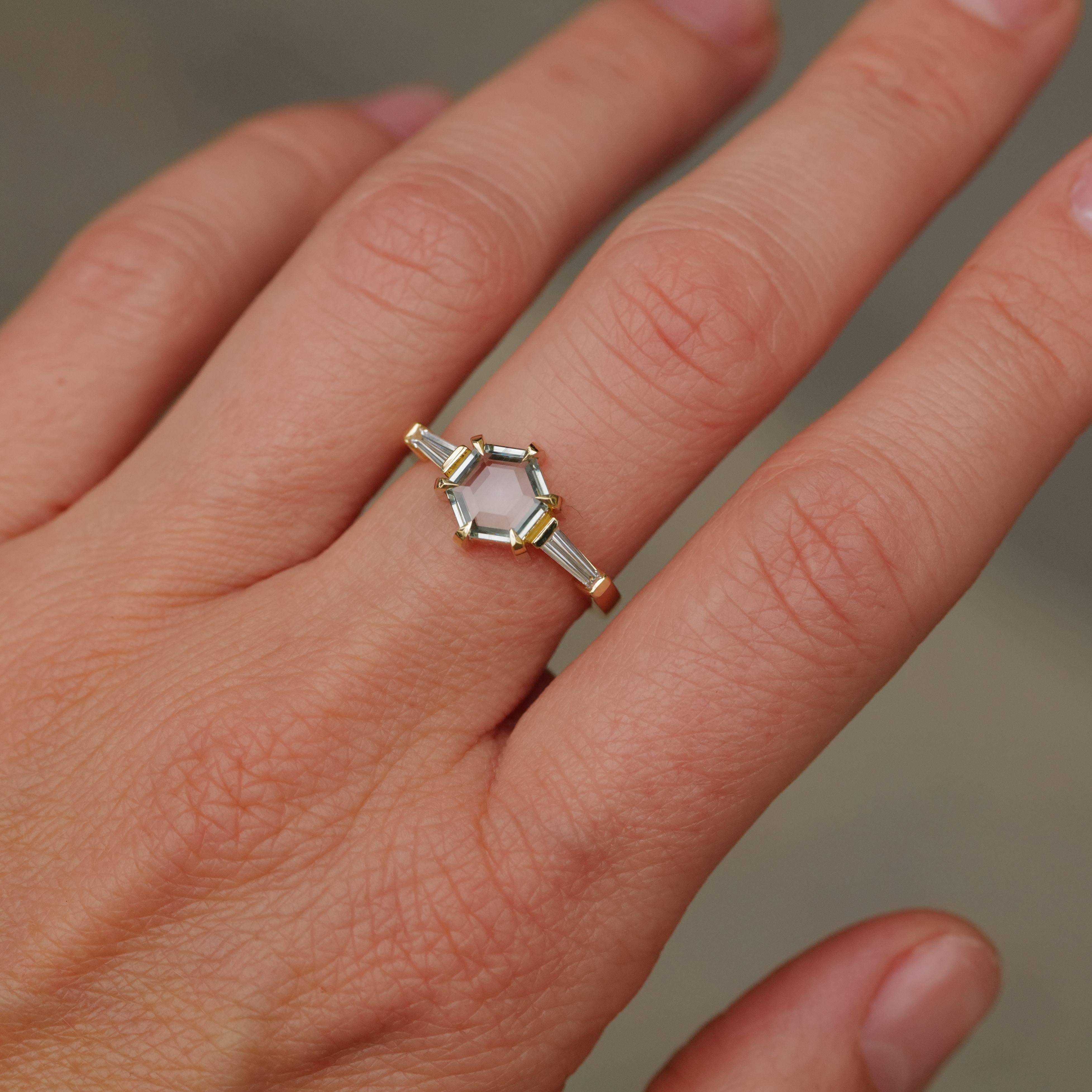 A hand wears the Fiat Lux Grande Calliope ring with a seafoam green hexagon sapphire and baguette diamond accents.