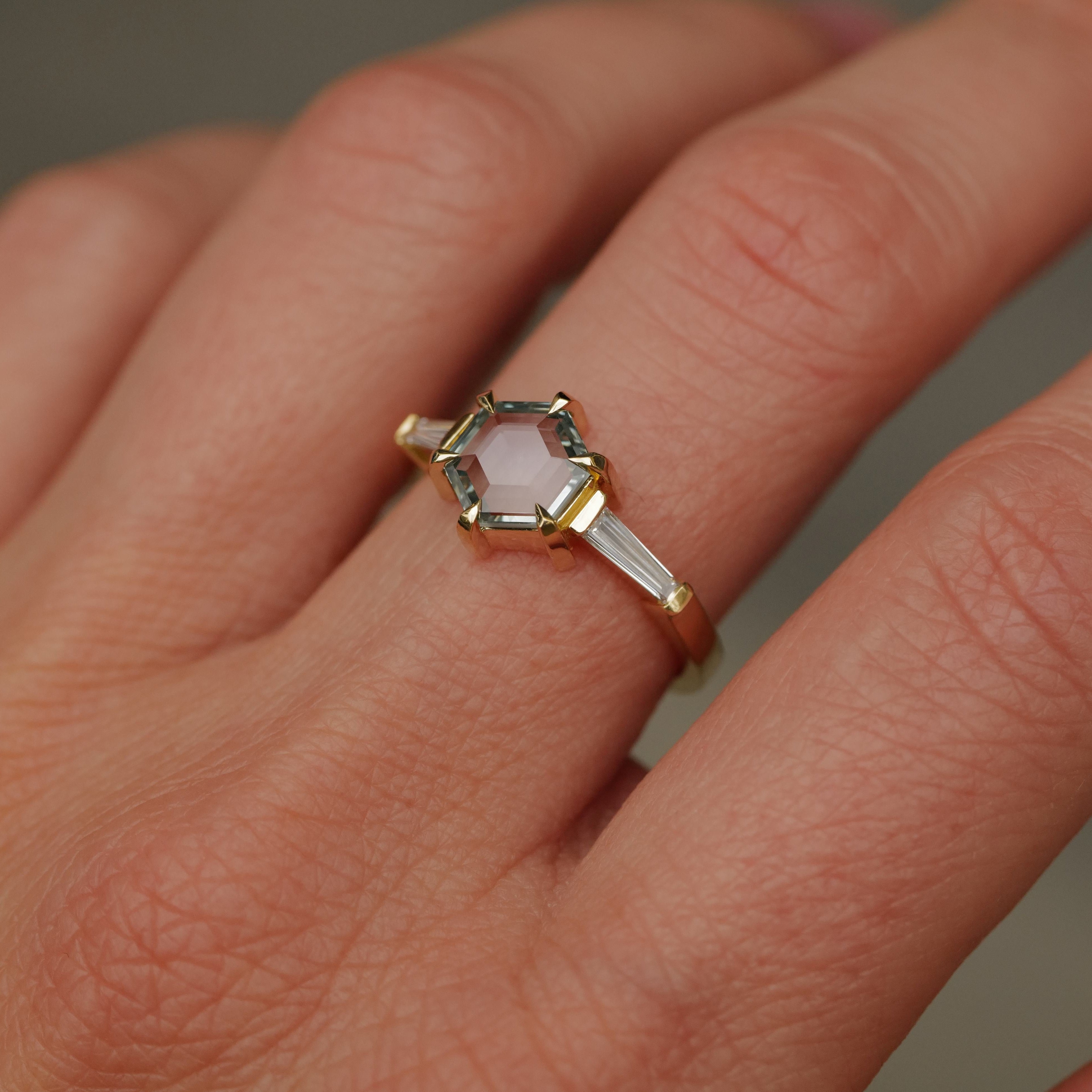 A hand wears Fiat Lux’s Grande Calliope ring, set with a seafoam green hexagon sapphire and baguette diamonds.