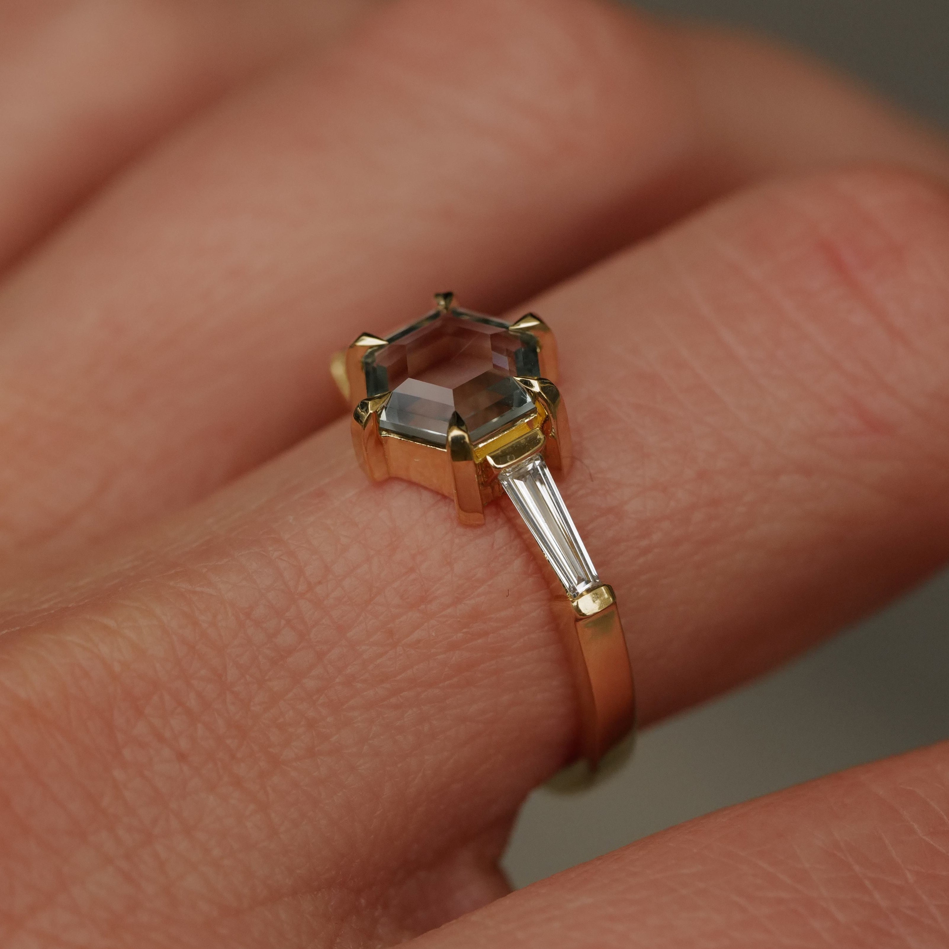 The Fiat Lux Grande Calliope ring features a 1.50ct seafoam green hexagon sapphire and tapered baguette diamond in 18K gold.