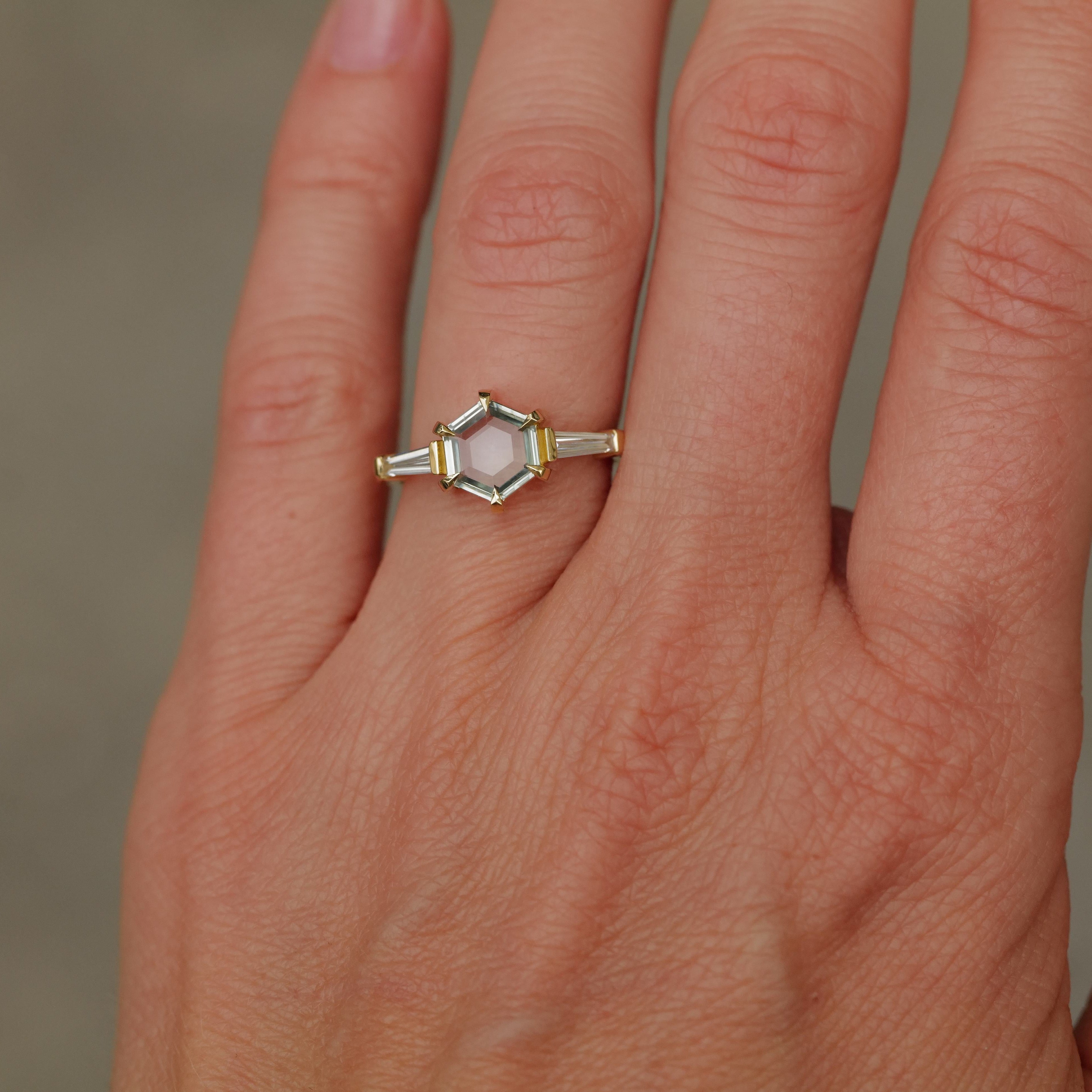 A hand wears Fiat Luxs Grande Calliope ring with a 1.50ct seafoam green hexagon sapphire and baguette diamonds.