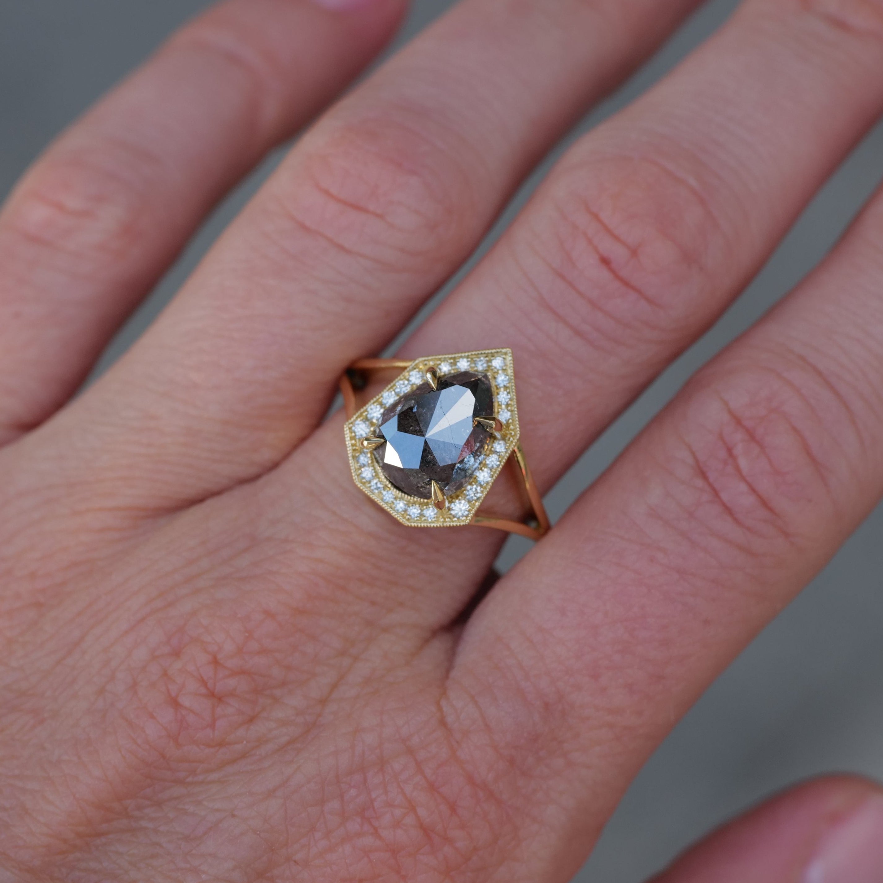 A hand wears Fiat Luxs Grande Phoebe 18K gold ring with a 4.88ct salt & pepper diamond and white teardrop diamonds.