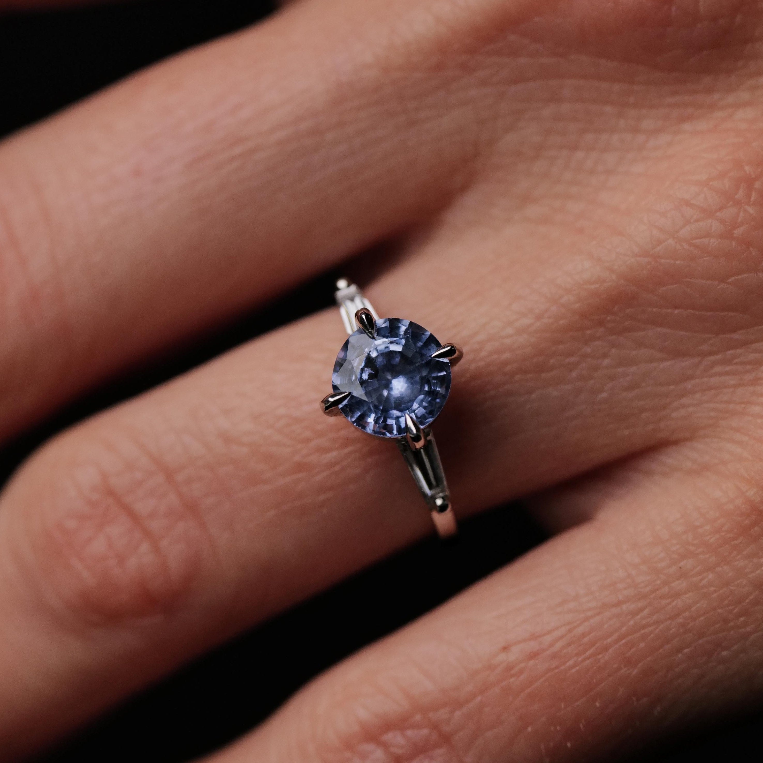 A hand wears the Grande Calliope - Periwinkle Blue Sapphire (2.05ct) platinum ring by Fiat Lux in a four-prong setting.