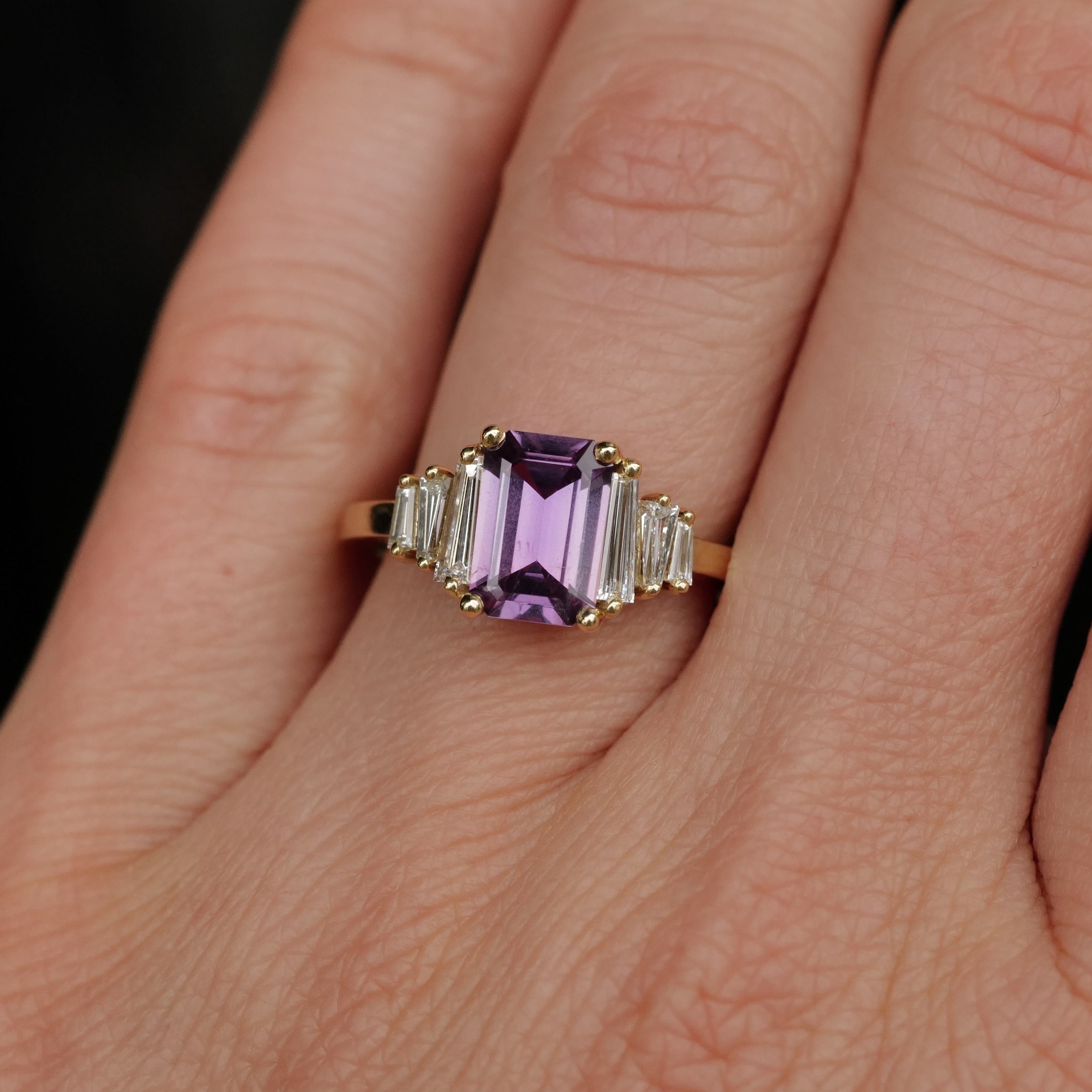 A hand wears the Fiat Lux Grande Calypso ring with a 1.94ct mulberry pink sapphire and diamond baguettes.
