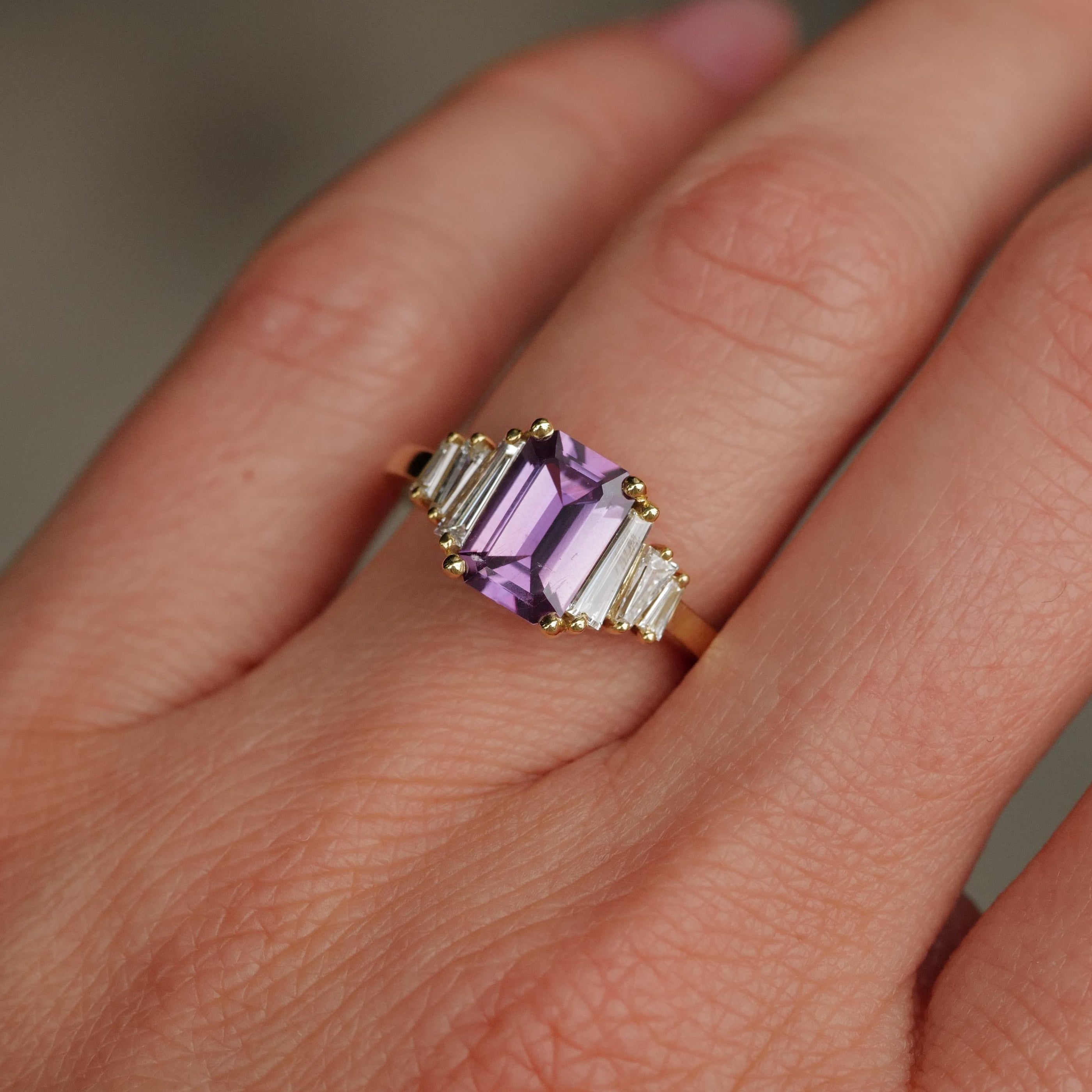 A hand wears Fiat Luxs Grande Calypso ring with a mulberry pink sapphire and tapered diamond baguettes.