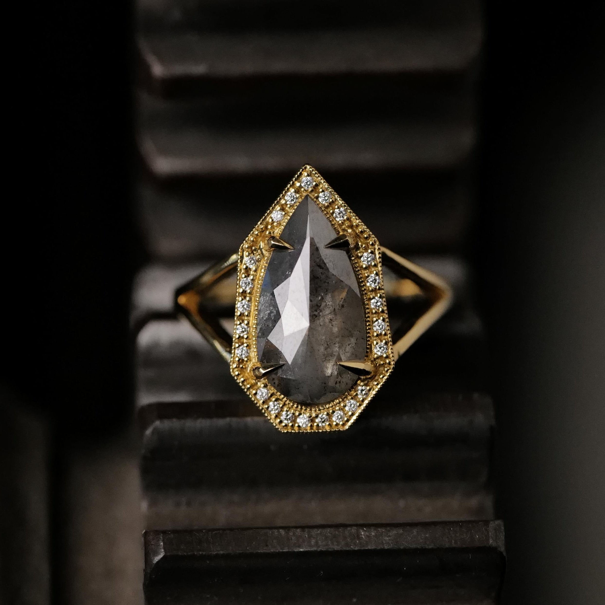 The Grande Phoebe Ring by Fiat Lux features a 2.34ct pear salt & pepper diamond with accent stones on a dark backdrop.