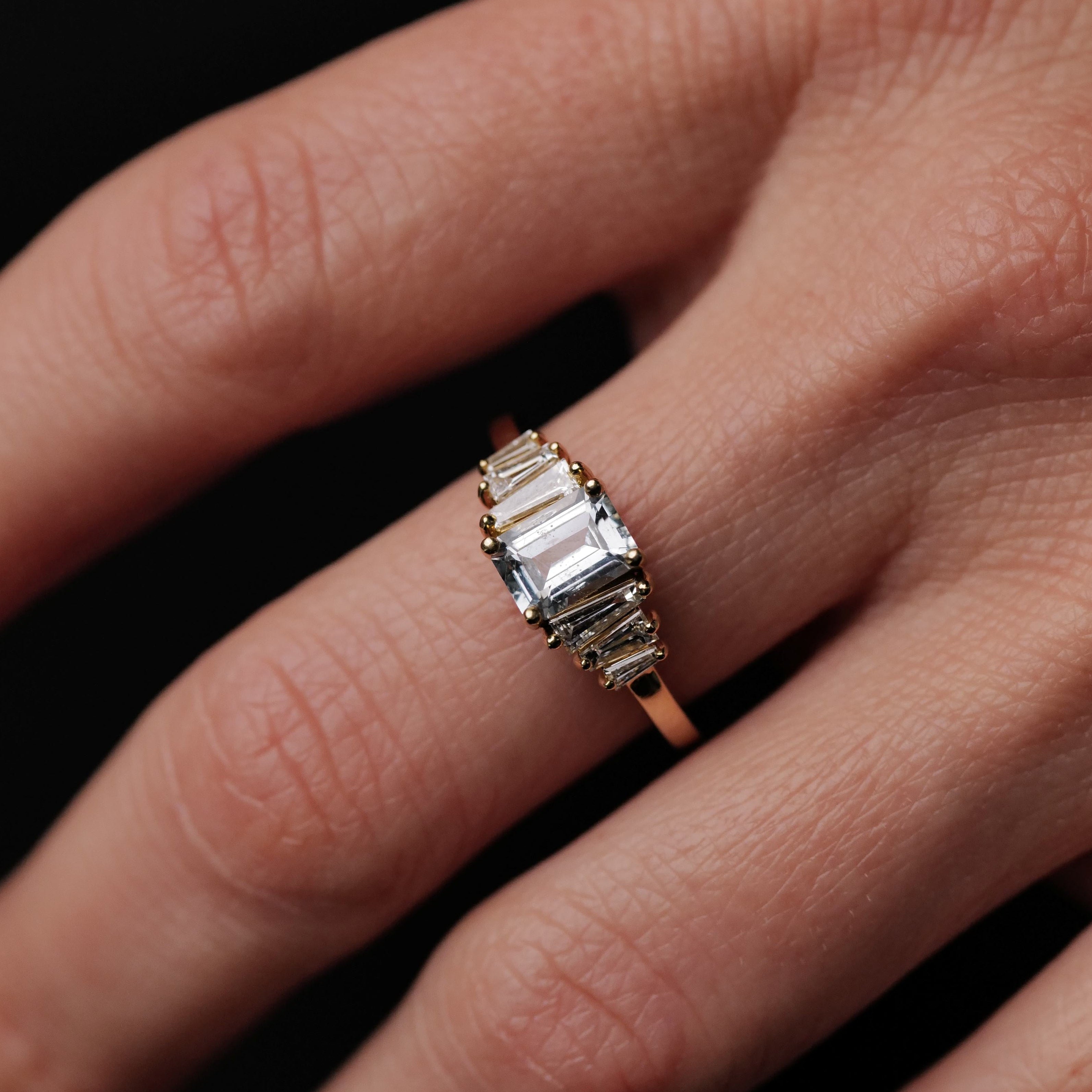 A hand wearing the Fiat Lux Petite Calypso ring, set with a row of 1.16ct ice blue sapphires.