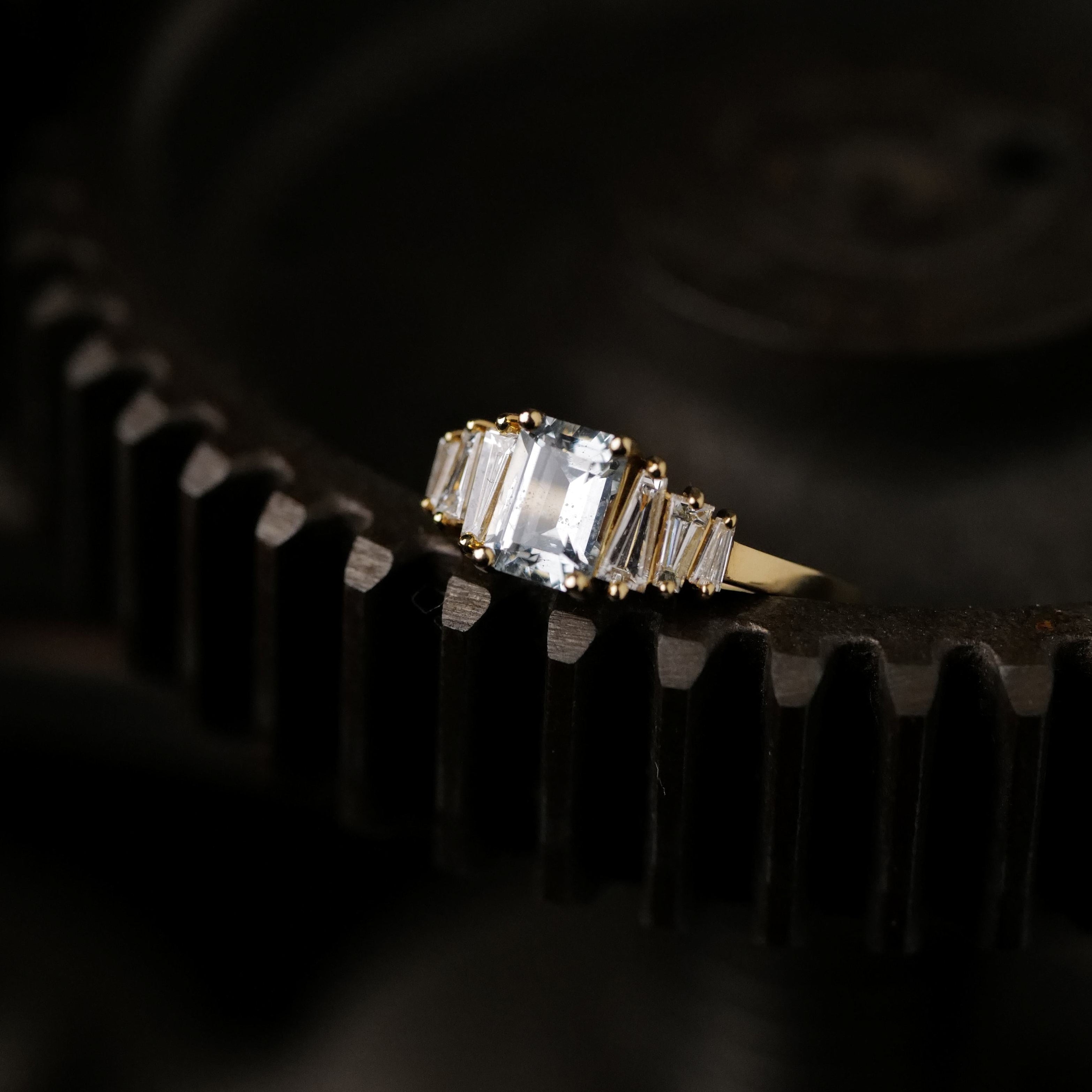 A Petite Calypso - Ice Blue Sapphire (1.16ct) ring by Fiat Lux rests on a dark metal gear.