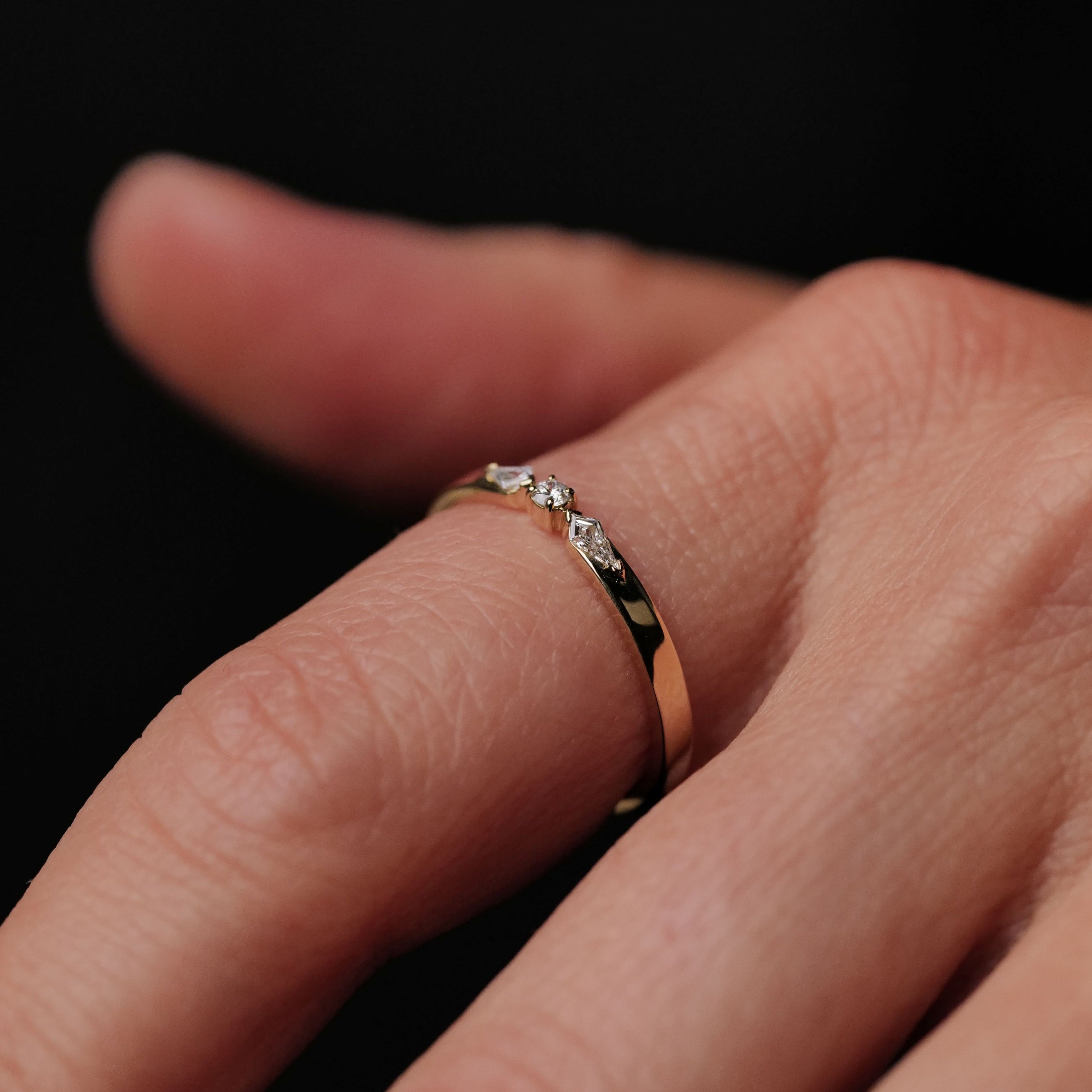 A Fiat Lux Petite Nova Ring in 14K gold with small diamonds is shown on a finger against a dark background.