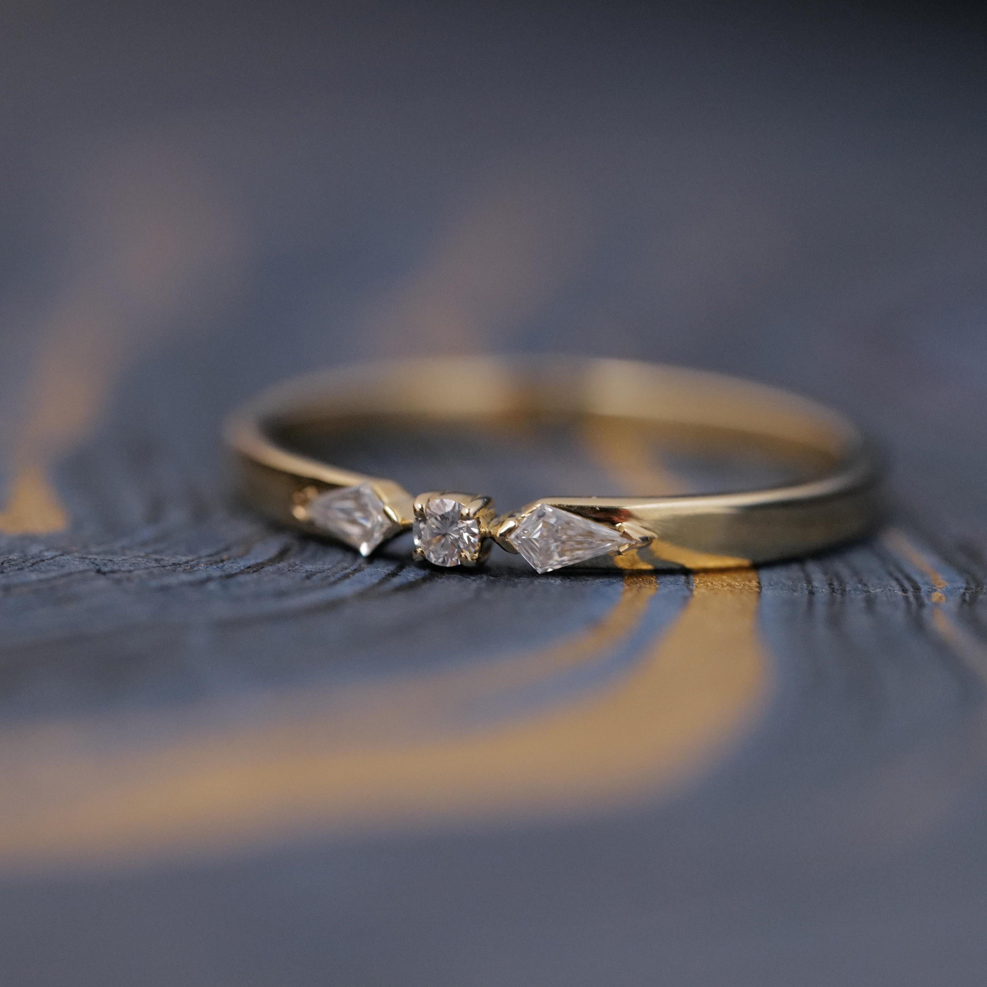 The Fiat Lux Petite Nova Ring in 14K gold with three diamonds, shown on a textured blue and gold surface.