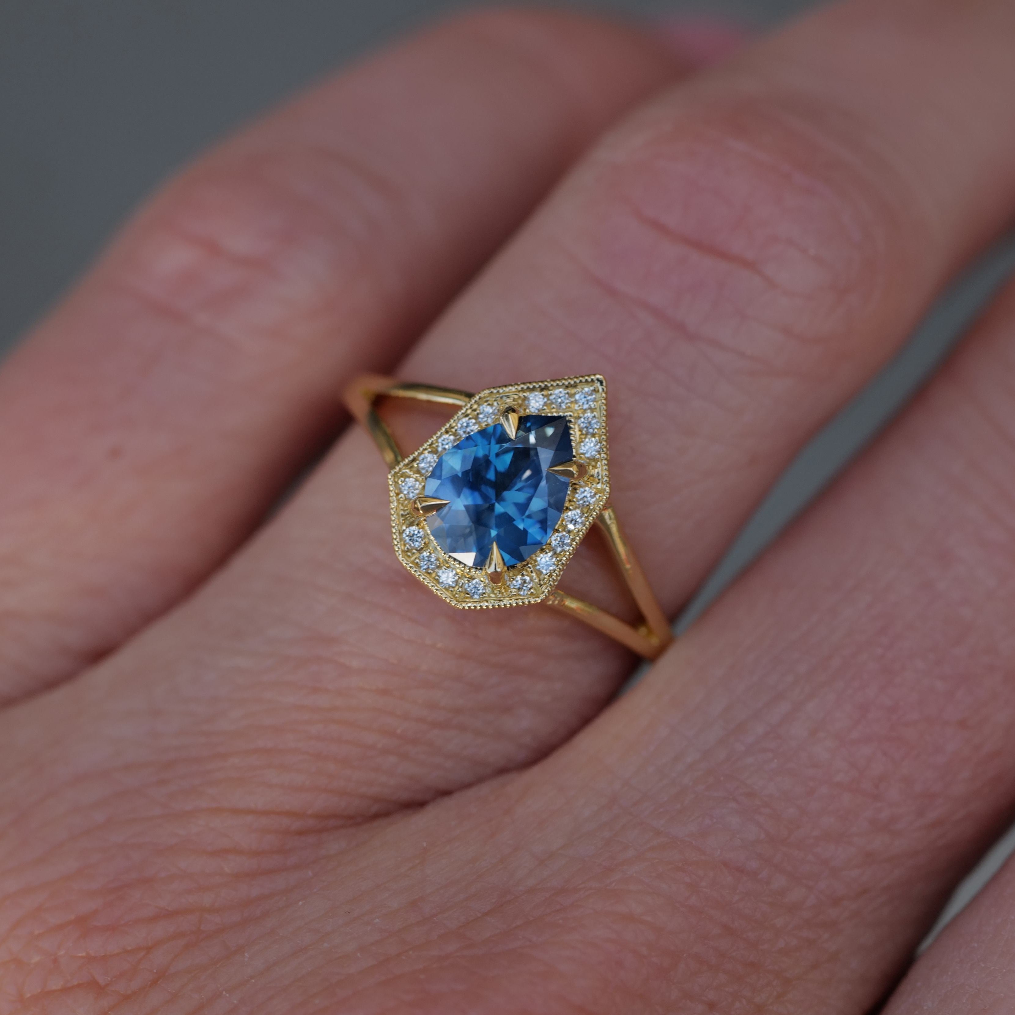 A hand wearing Fiat Luxs Petite Phoebe, a pear-cut denim blue Montana sapphire ring with a diamond halo.