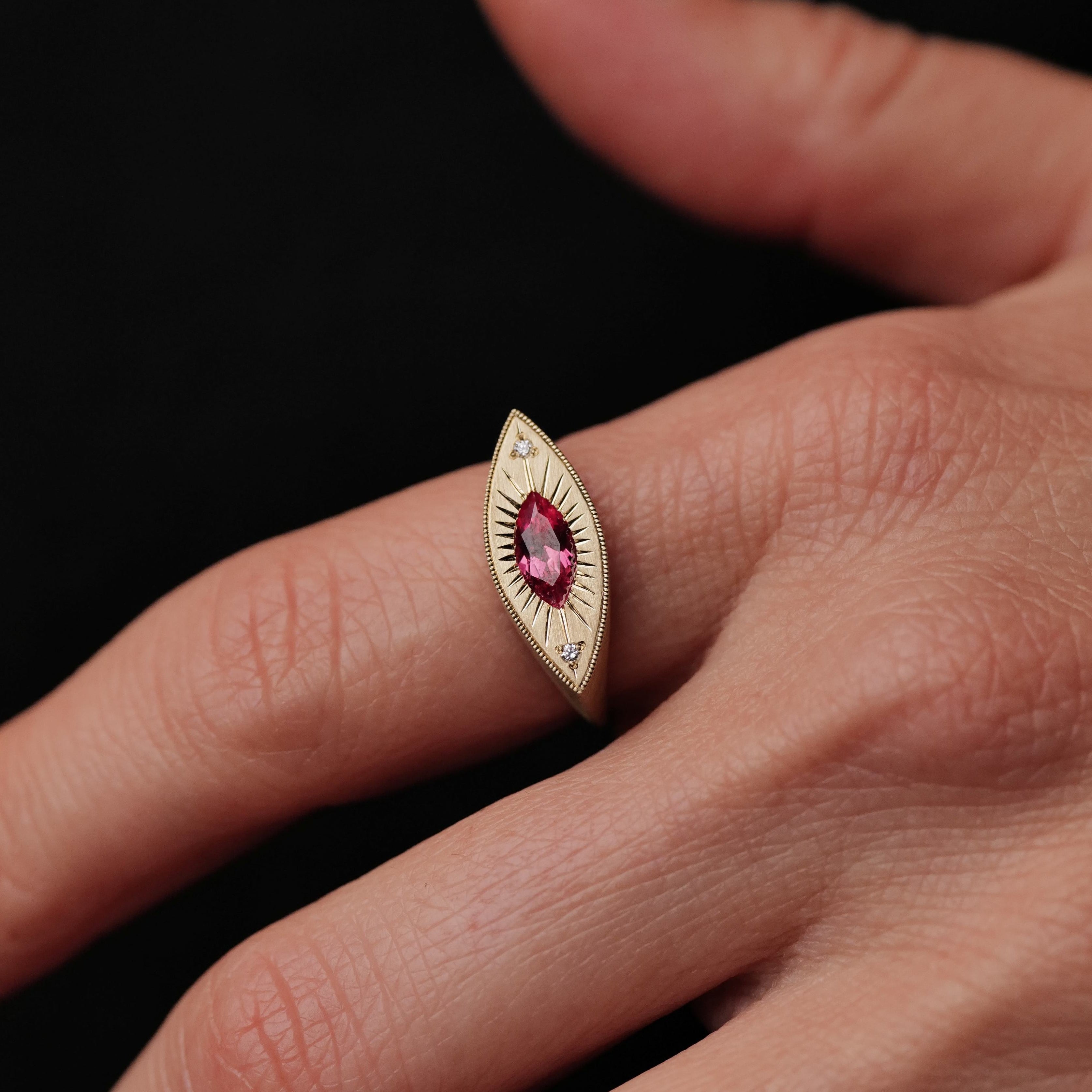 A hand wears Fiat Luxs Brilliant Third Eye ring with a 0.63ct Summer Coral Sapphire and two diamonds on black.
