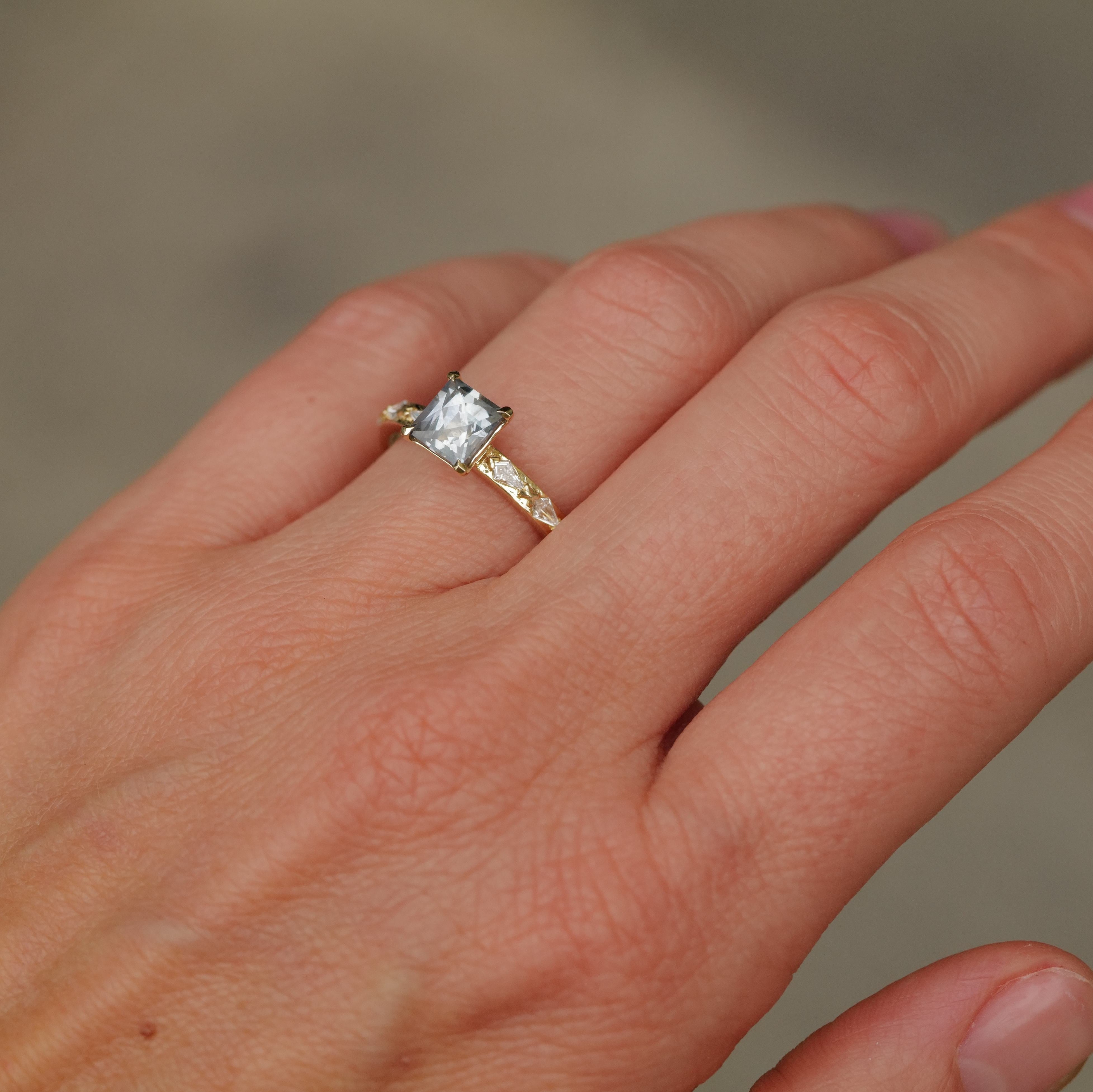 A hand models the Fiat Lux Classic Theia Ring—14K gold with a 1.41ct rectangular aqua sapphire, on a neutral backdrop.