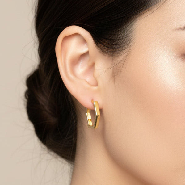 Woman with smooth skin, natural makeup, and neat low bun wears Fiat Lux Grande Hexagon Huggie Hoop earrings.