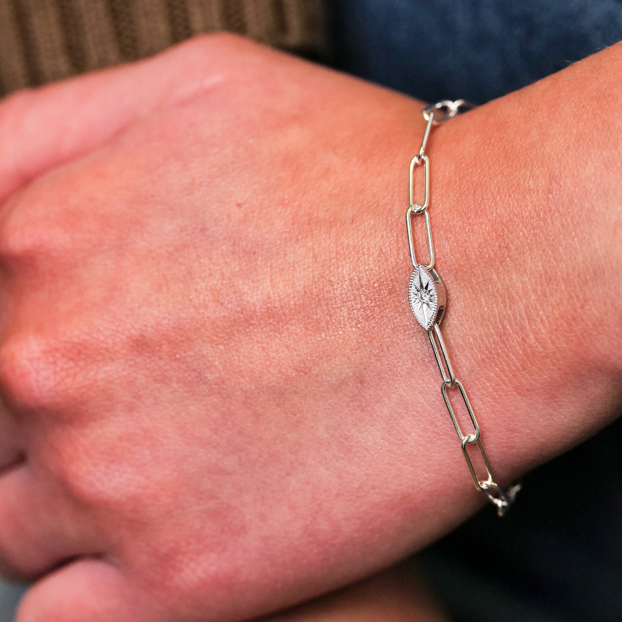 Close-up of a hand wearing Fiat Luxs Grande Mati Bracelet (G)—a silver chain with an engraved oval charm.