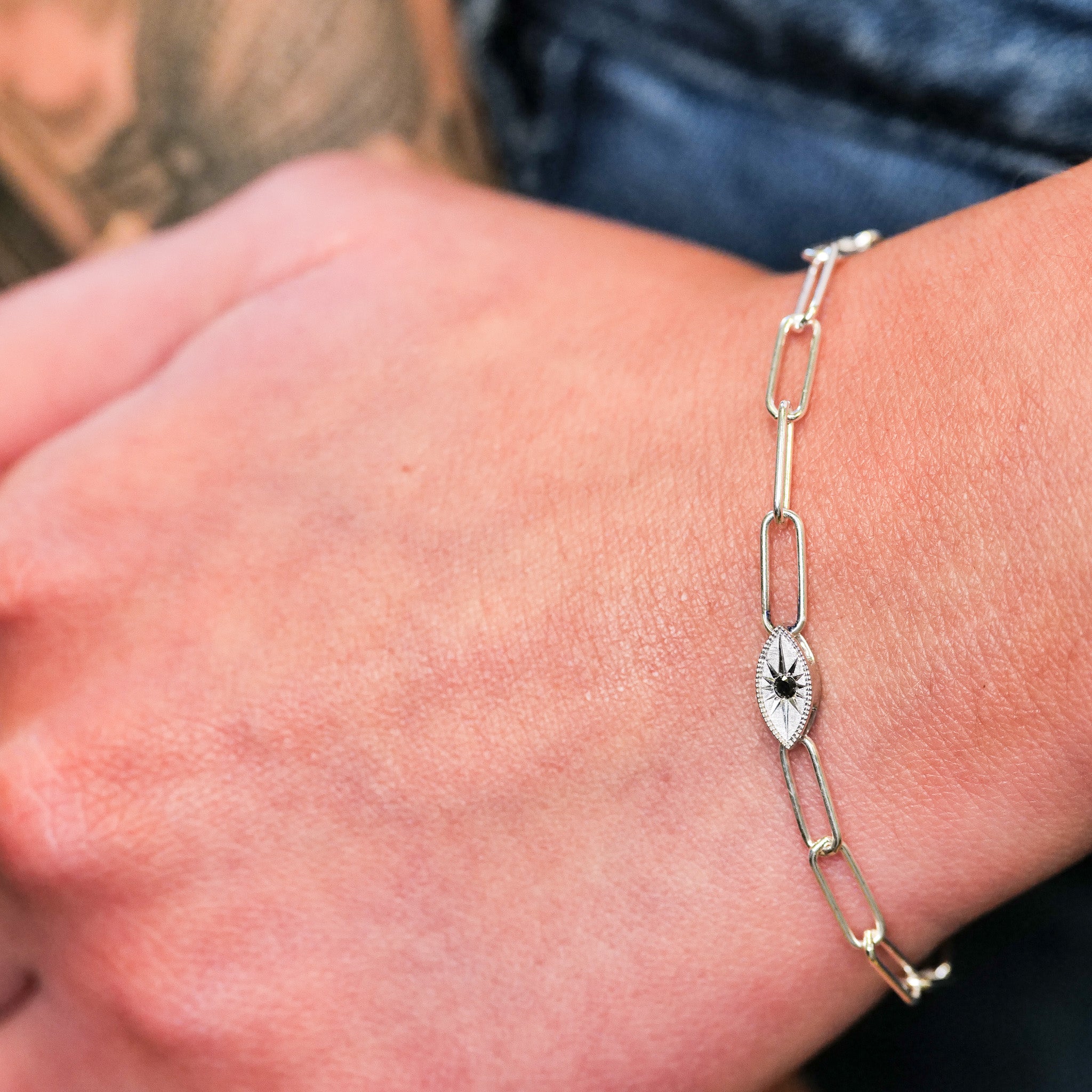 Close-up of a hand wearing the Grande Mati Bracelet (G) by Fiat Lux, a delicate silver chain with an engraved oval charm.
