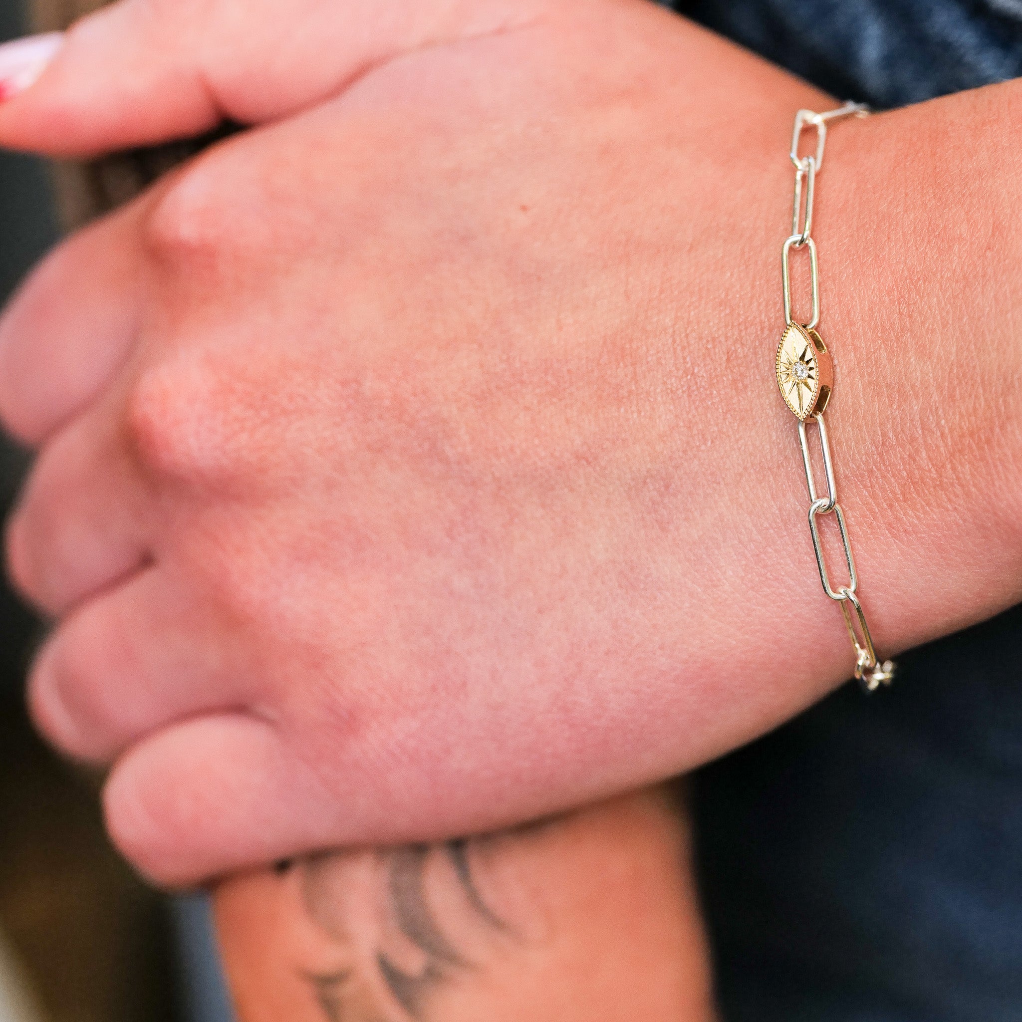 A close-up of a hand wearing Fiat Lux’s Grande Mati Bracelet (G), a minimalist gold chain with a 14K gold charm.