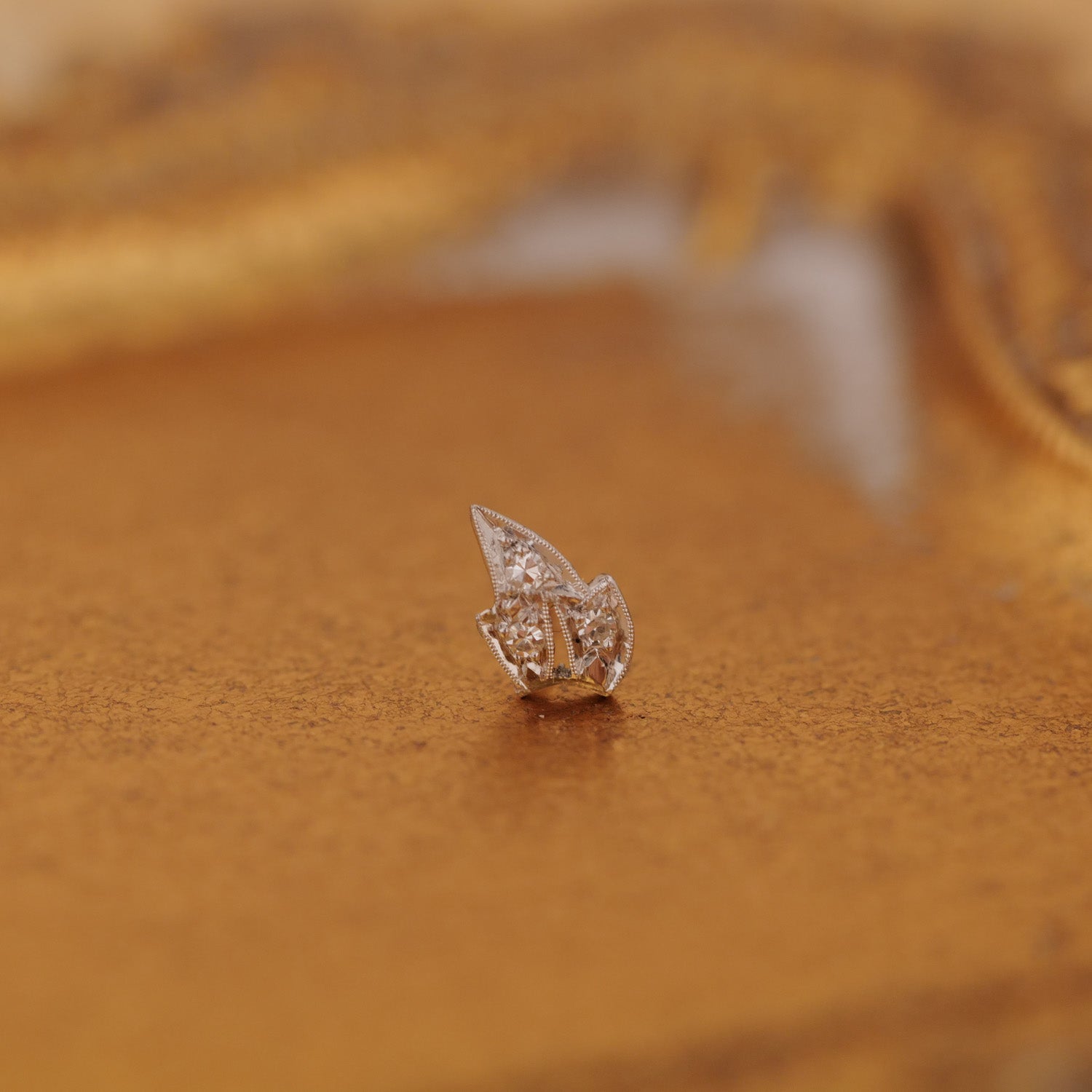 A Vintage Platinum Leaf Earring with diamond detailing rests on a reflective platinum surface.