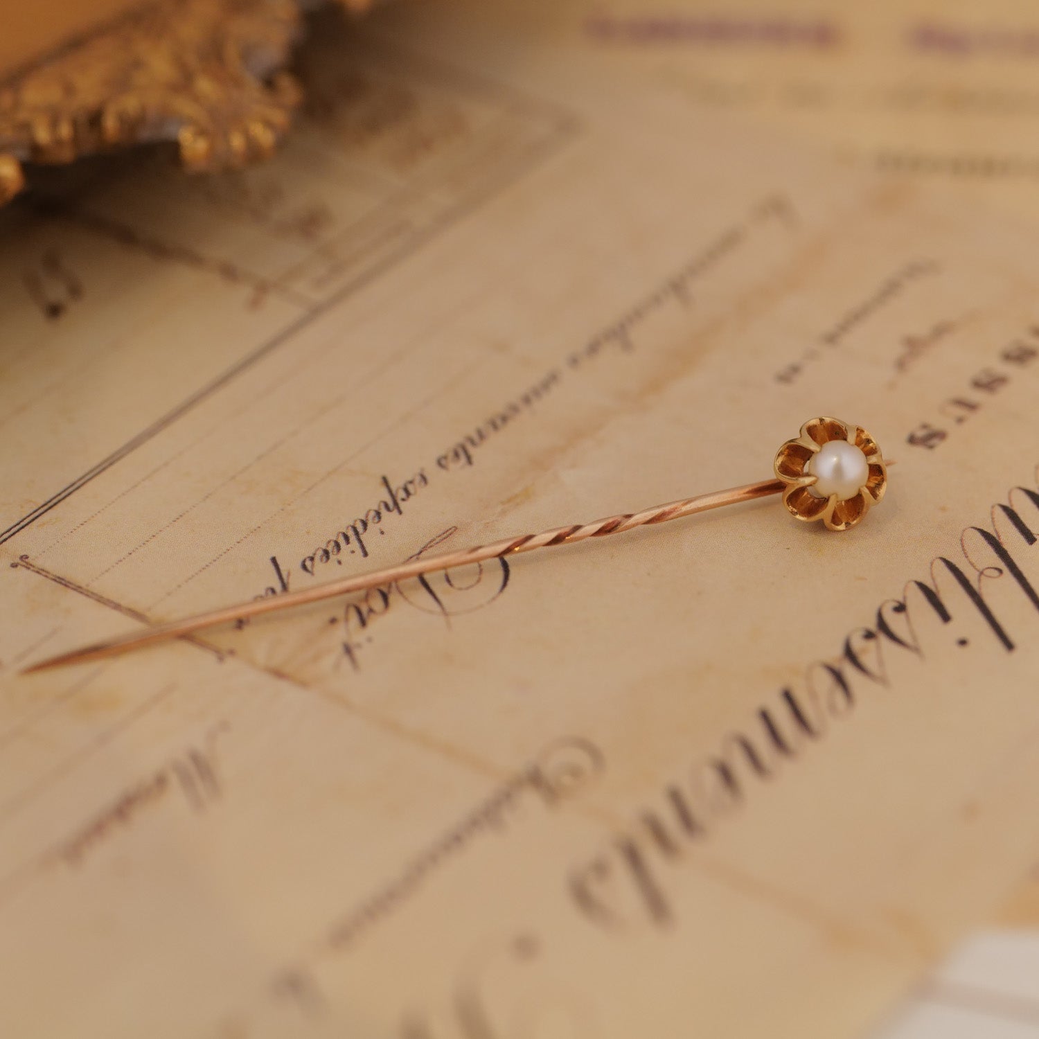 The Vintage Antique Pearl Belcher Stick Pin in 14k rose gold rests on vintage handwritten paper.
