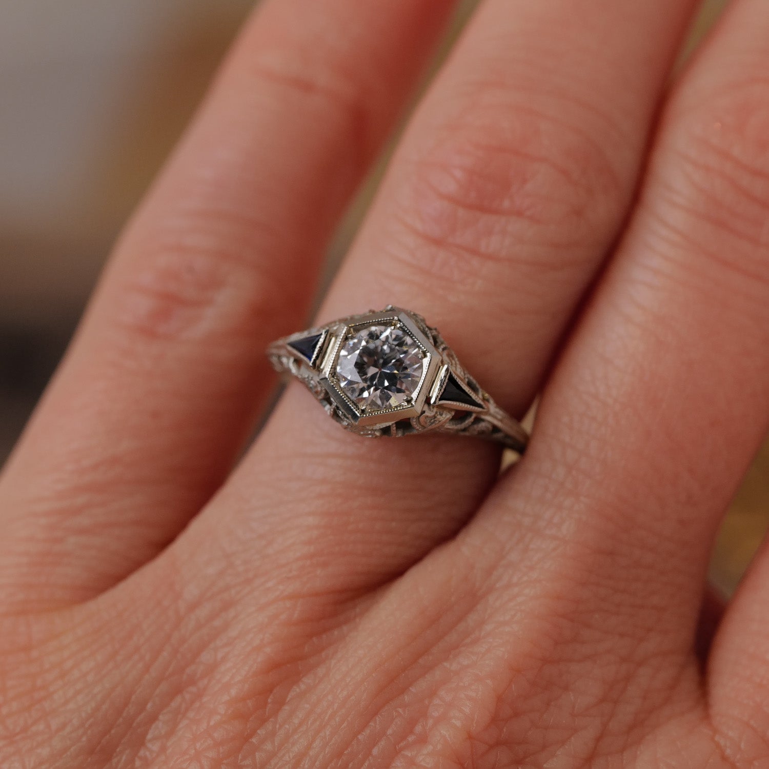 A hand wears Vintages Art Deco Botanical Hexagon Ring, featuring an Old European Cut diamond and ornate band accents.