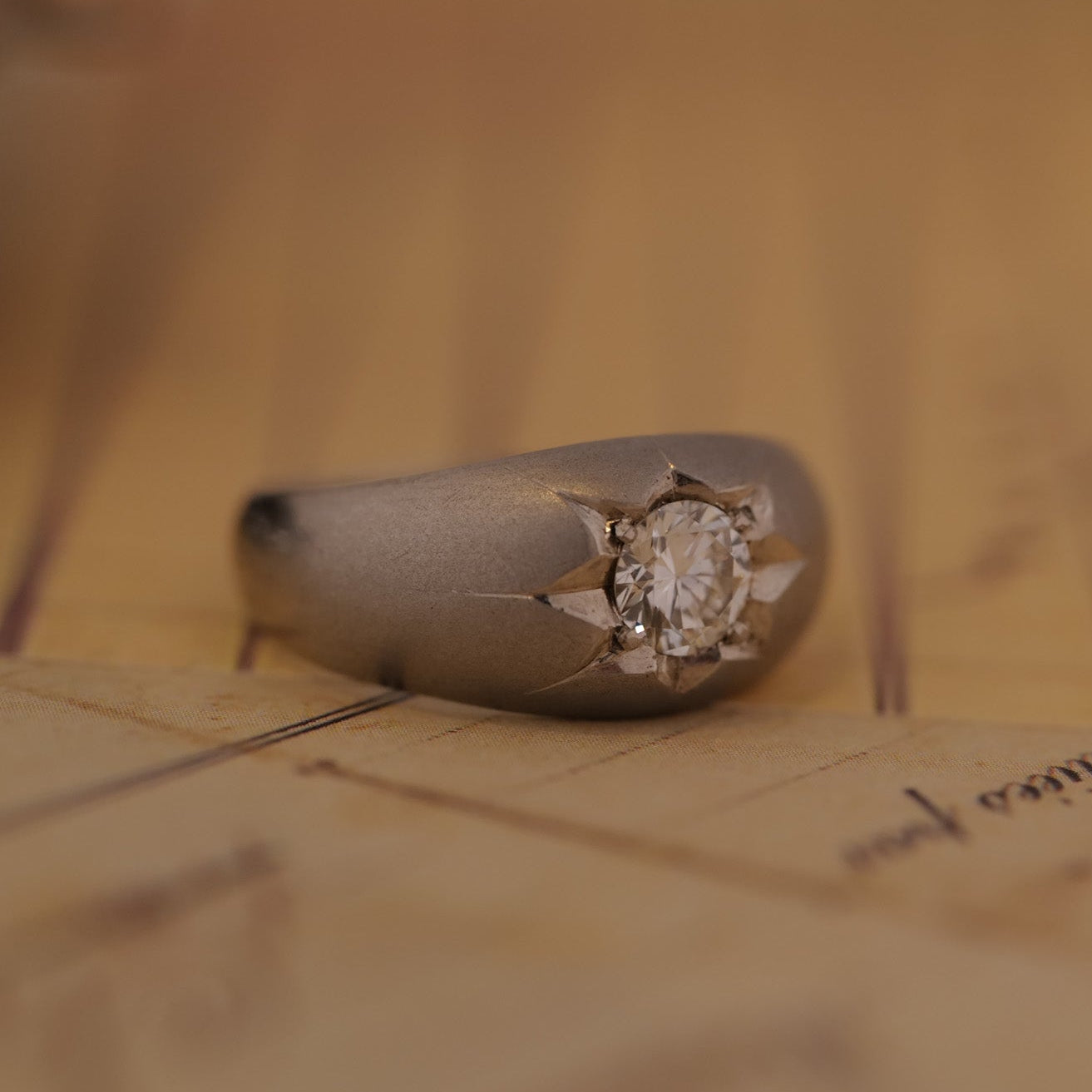 The Vintage Star Set Diamond Platinum Ring features a round diamond on a blurred script background.