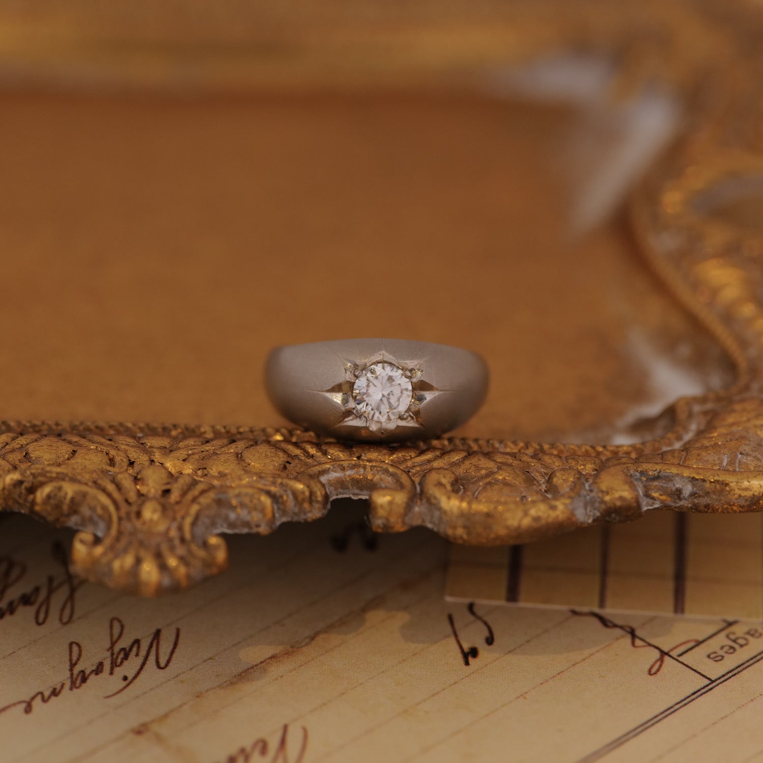The Vintage Star Set Diamond Platinum Ring gleams atop an ornate frame, handwritten papers beneath.