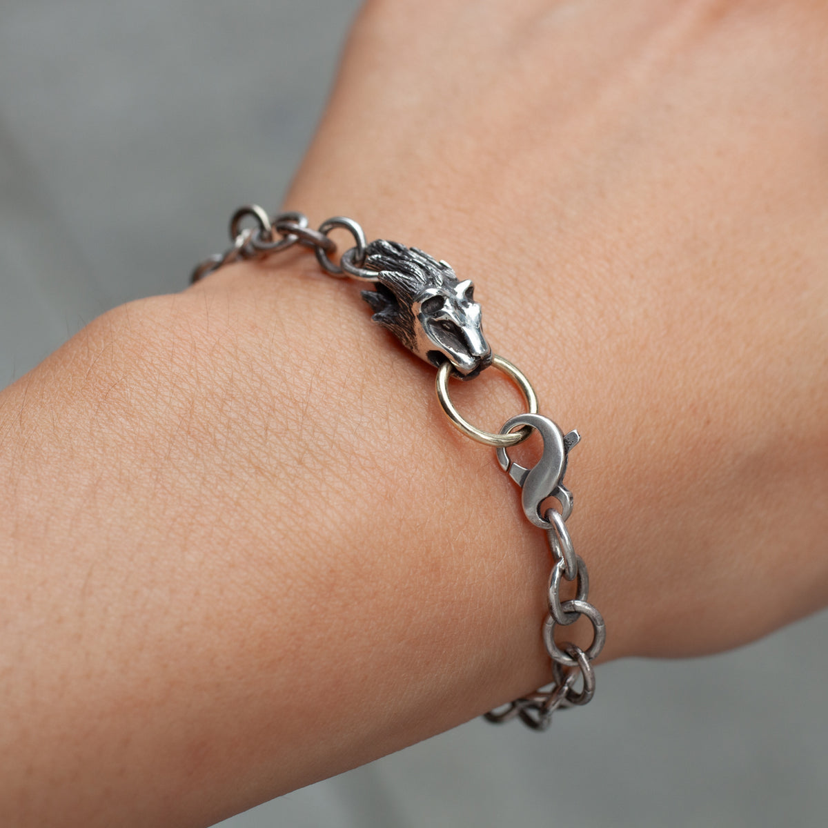 The Reign Bracelet by Allison Bartline, featuring a wolf head clasp, is worn on a person’s wrist.
