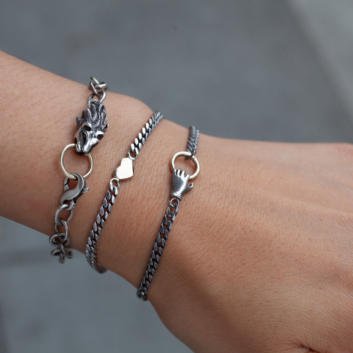 Three Acanthus Fob Grip sterling silver bracelets: dragon, heart, and hand clasp with a 14K gold ring.
