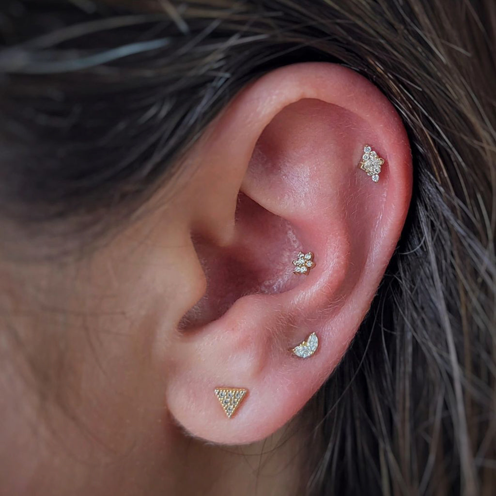 A close-up of an ear with four yellow gold labret piercings, featuring an Embrace Marquise diamond stud.