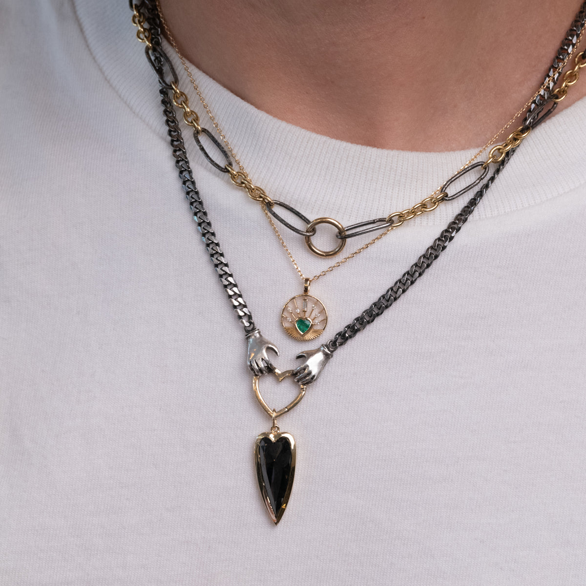 Three layered 14K gold necklaces, including a Celine Daoust Heart Medal Necklace - Emerald, and a black heart pendant.