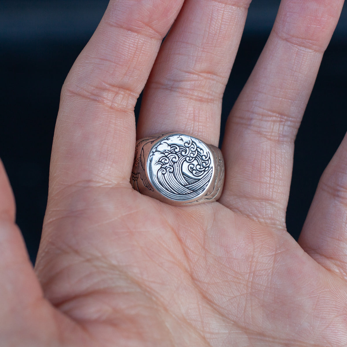 The Great Wave Signet Ring in sterling silver on a finger, featuring an engraved Hokusai wave design.