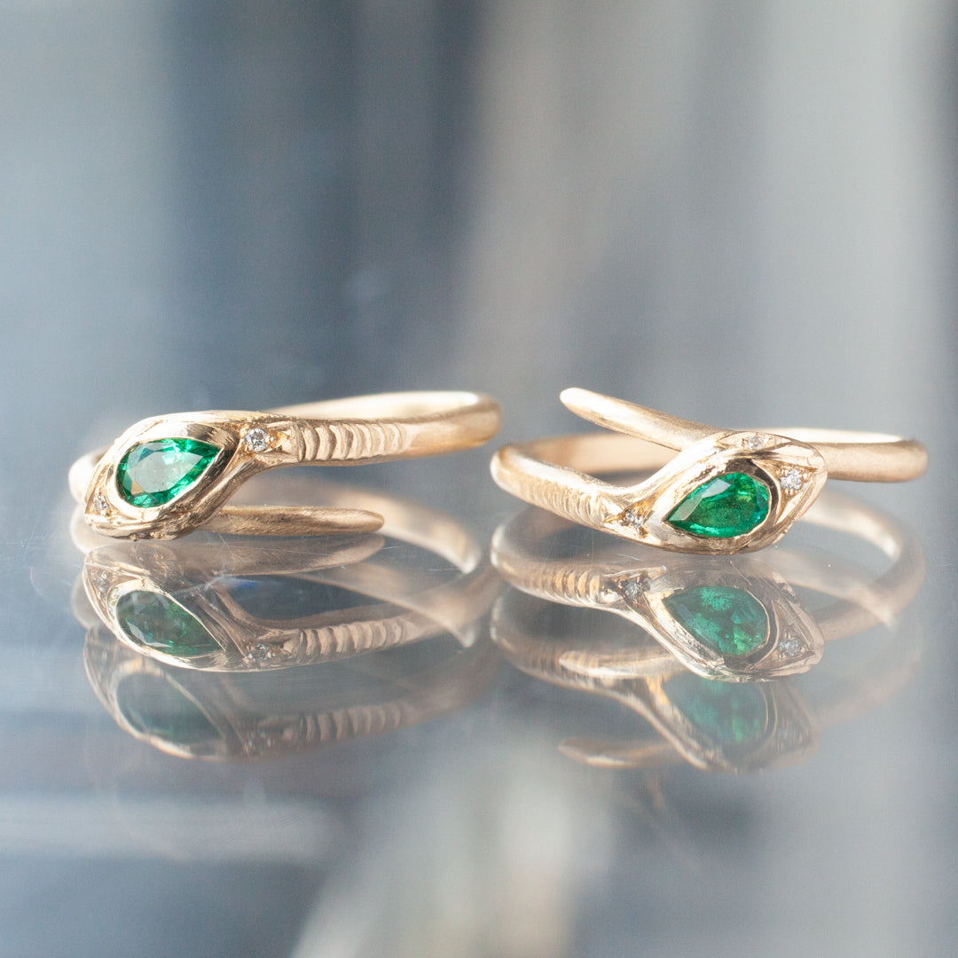 Two Victorias Fede Ring - Emerald Pear by Daisy San Luis, with emerald accents, displayed on a reflective surface.