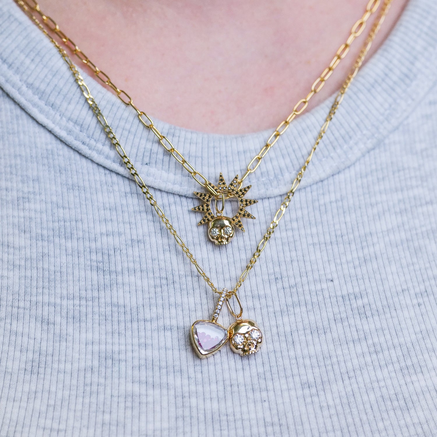 Three Fiat Lux 14k gold necklaces, incl. The Skull Charm - Grande, layered on a light blue ribbed shirt.