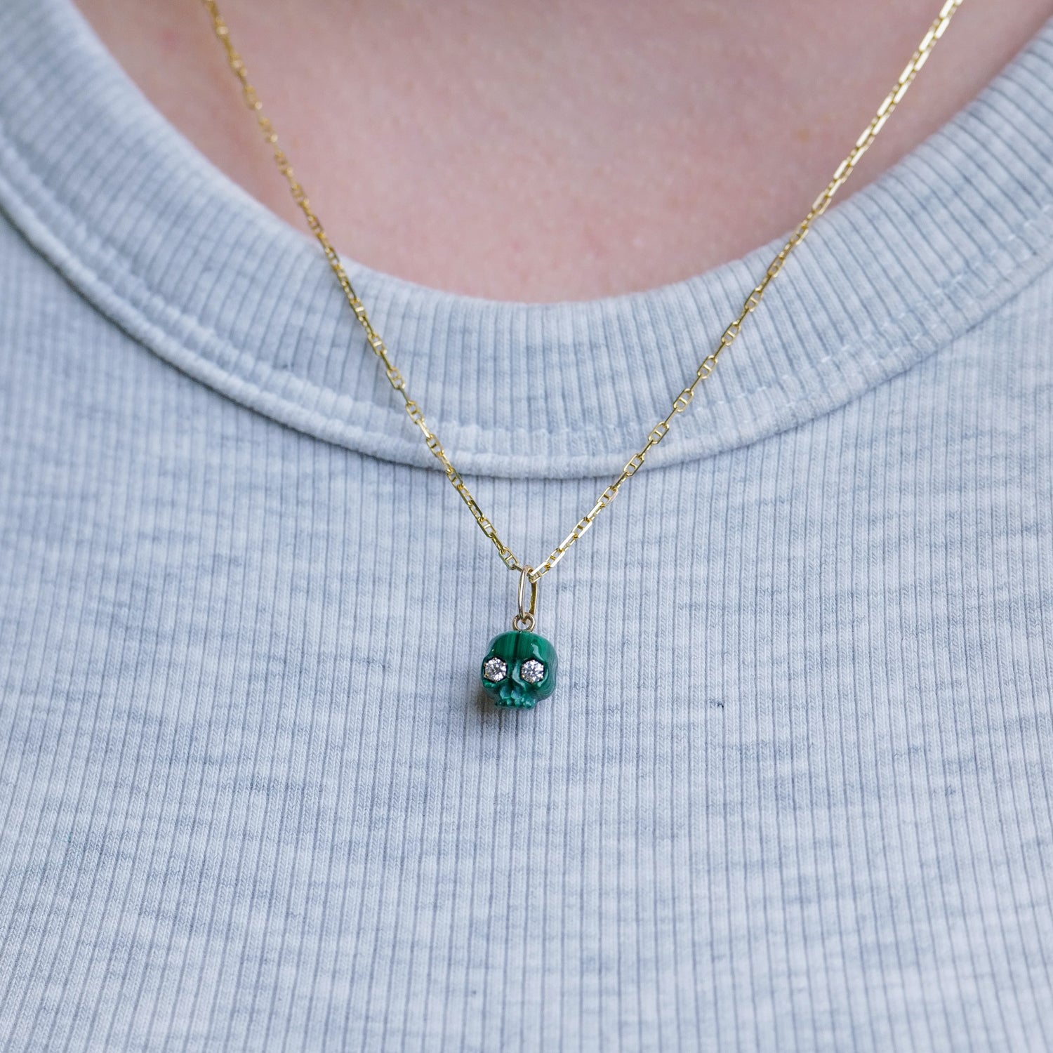 Fiat Lux The Skull of Bloodstone diamond skull and green pendants over a light blue ribbed shirt.