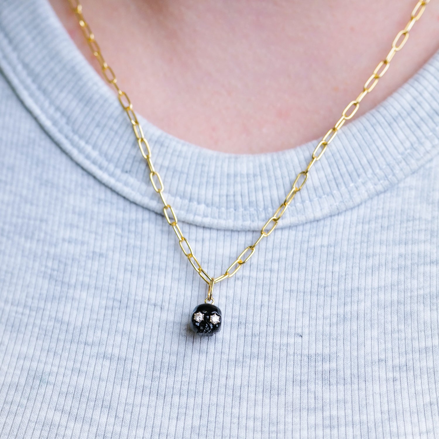 Fiat Lux’s The Skull of Onyx gold necklace with onyx skull charm, styled over a light gray ribbed shirt.