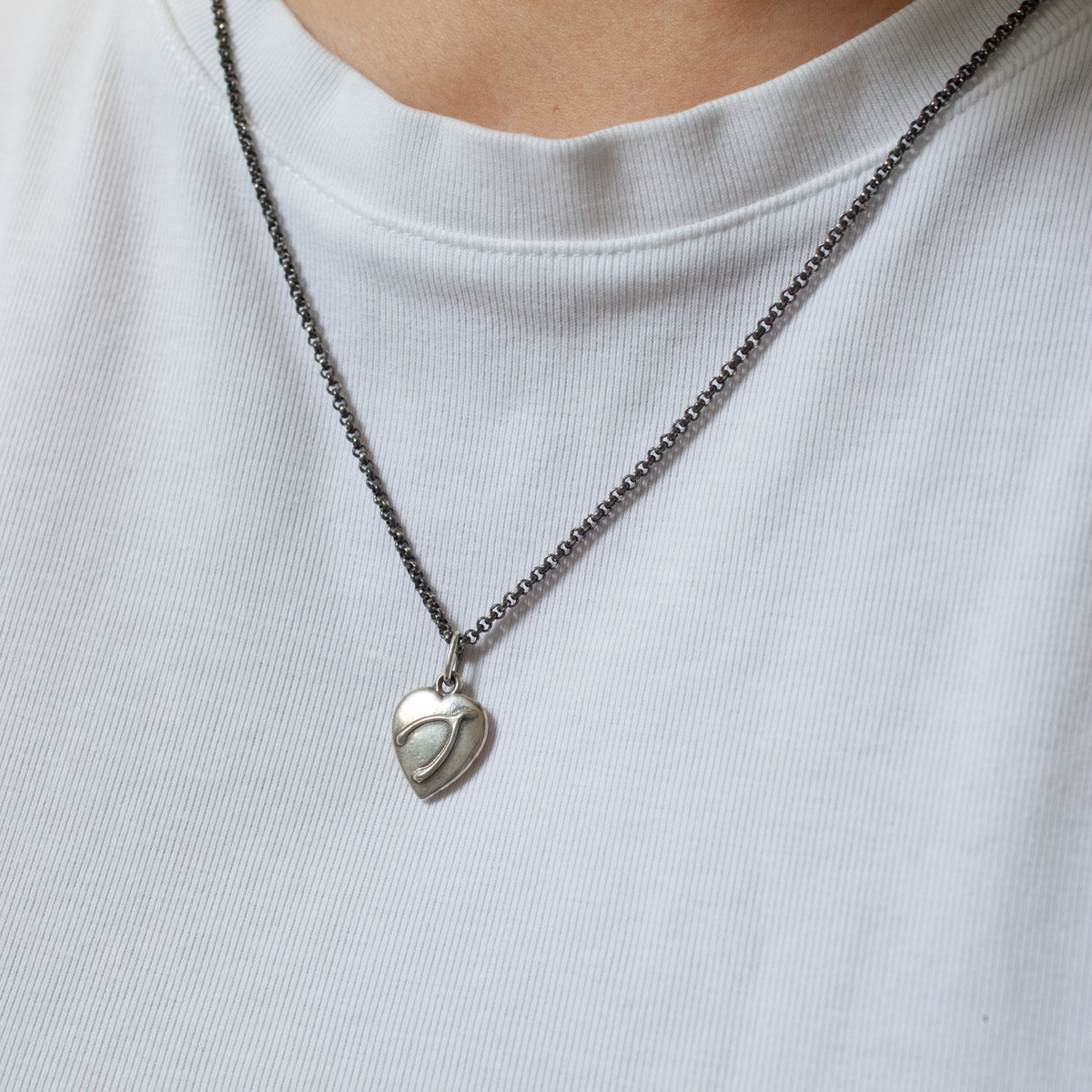 Fiat Lux Wishbone Heart Charm (S) on a dark chain, styled over a white ribbed shirt.