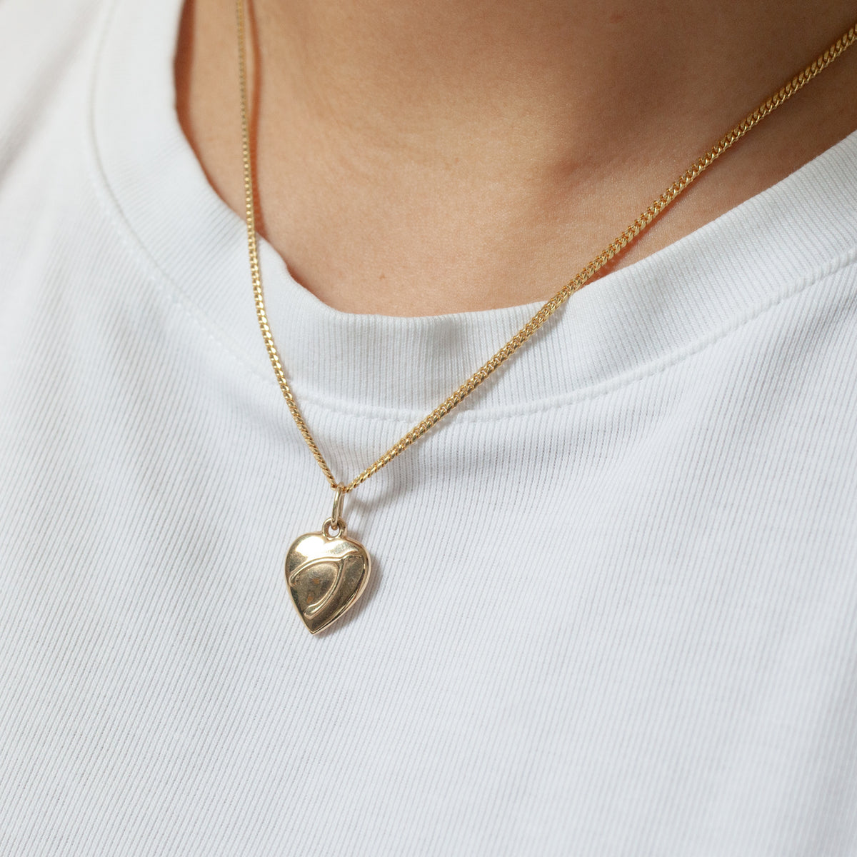 A Fiat Lux Wishbone Heart Charm (G) shines on a neck, styled with a white ribbed shirt for timeless sophistication.